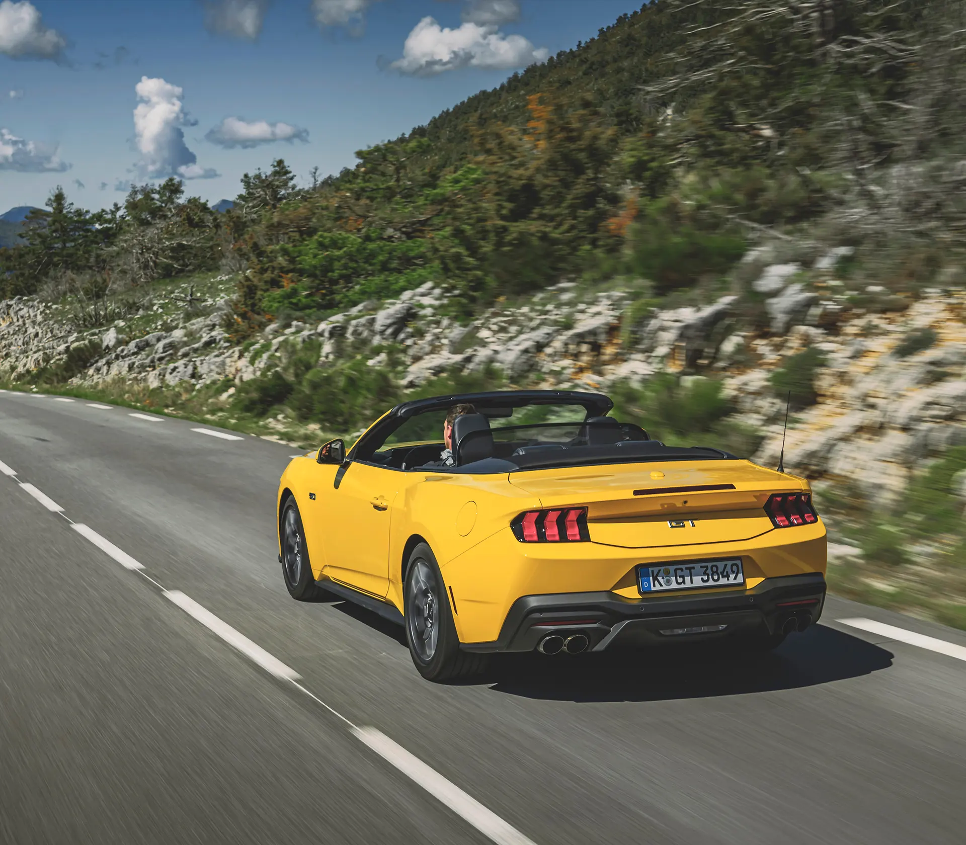 Heckansicht auf gelber Mustang als Cabrio fährt auf einer kurvigen Straße