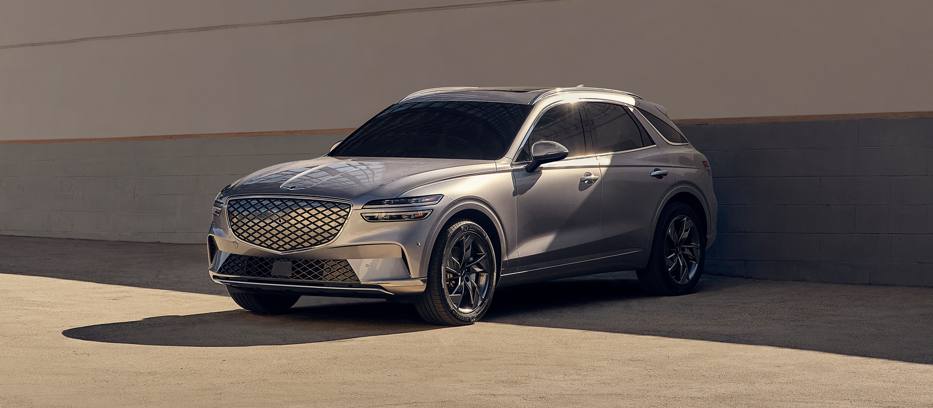 Genesis Electrified GV 70 in grau steht vor einer weiß/grauen Wand geparkt mit dem Heck zur Wand gerichtet.