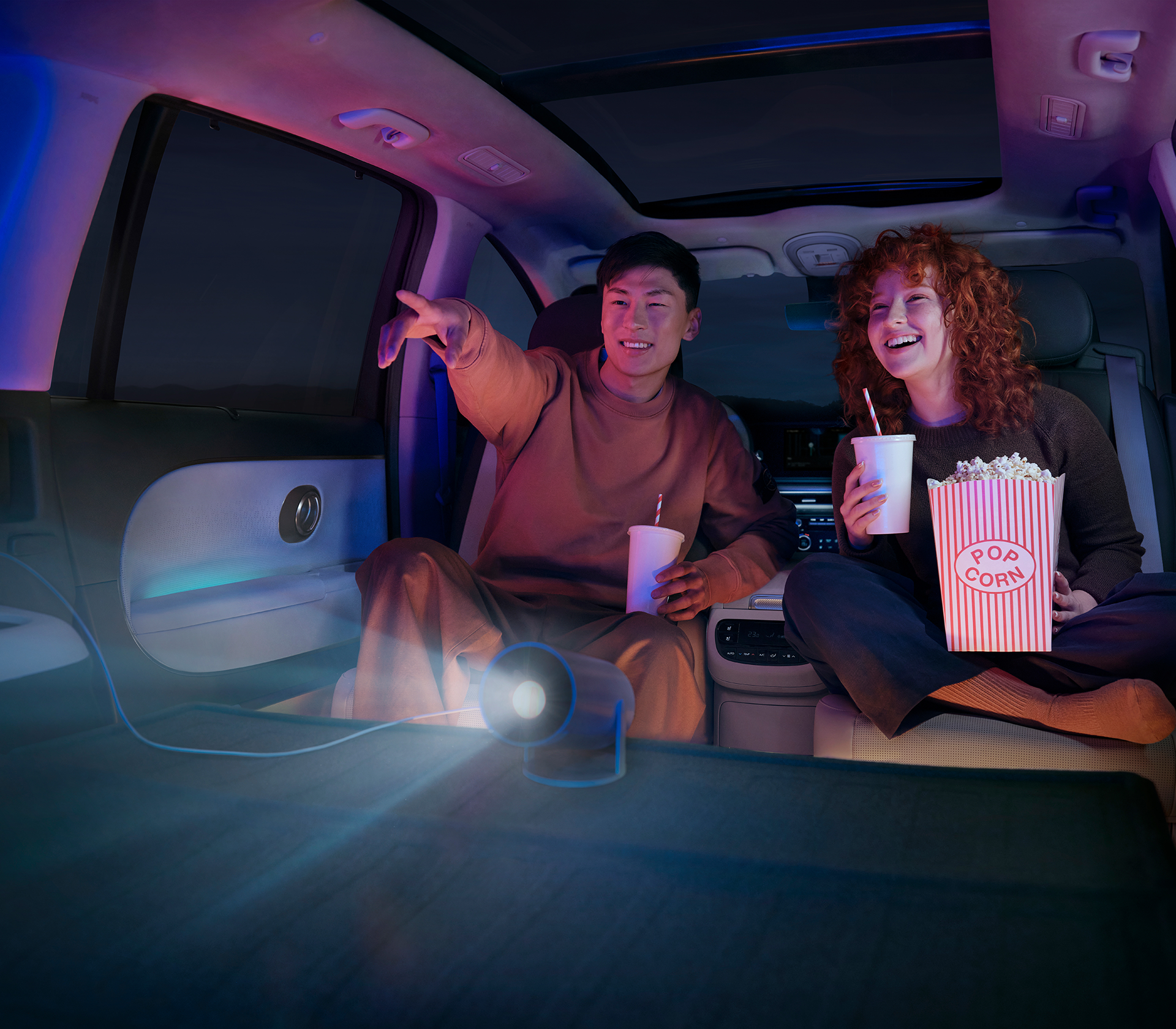 Hyundai IONIQ 9 zwei MEnschen im verdunkelten Innenraum, die mit einem Beamer einen Film gucken und Popcorn und Getränke haben