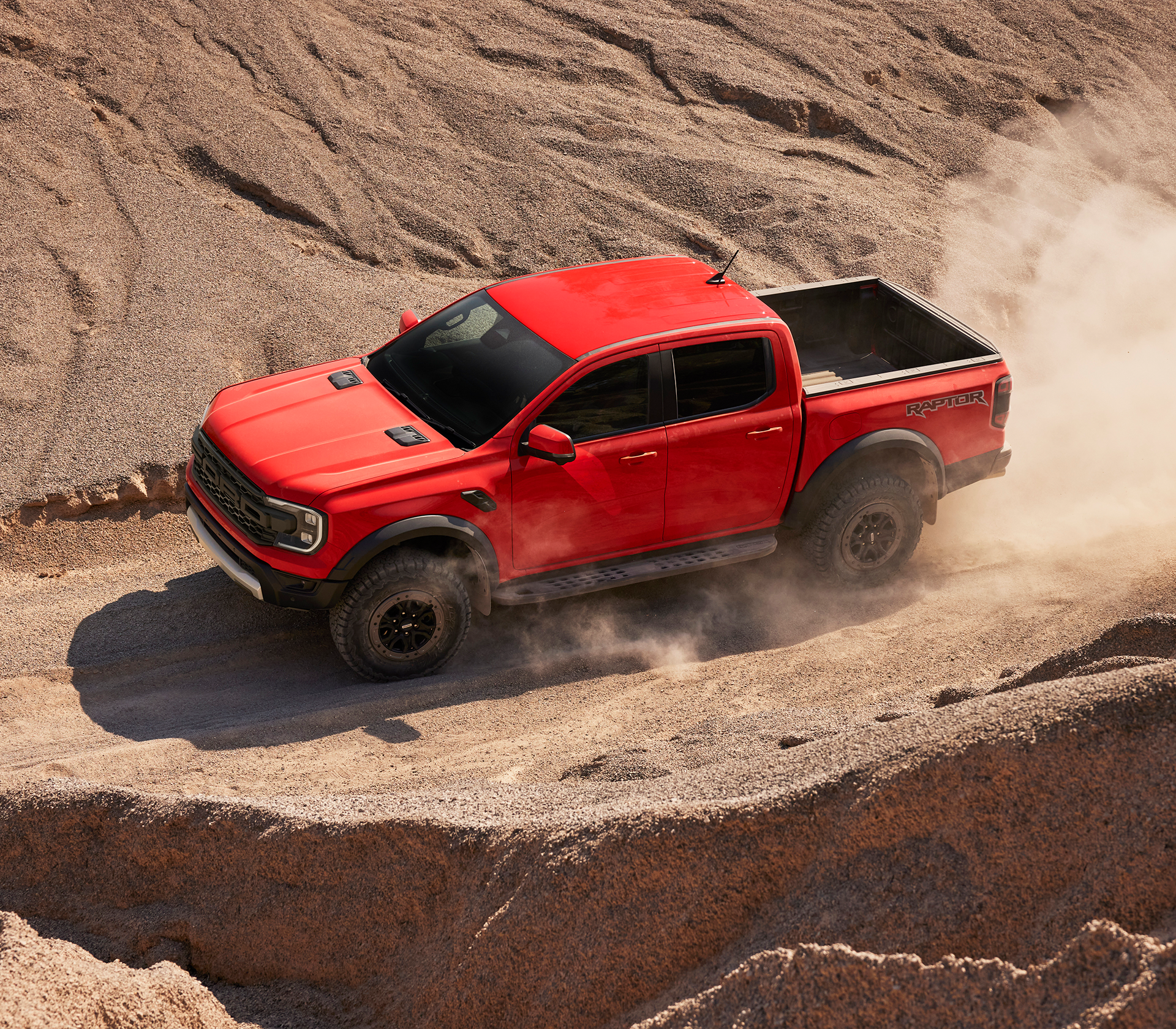 Ford Ranger Raptor Terrain in rot fährt offroad in einerm hügeligen und sandigen Gelände