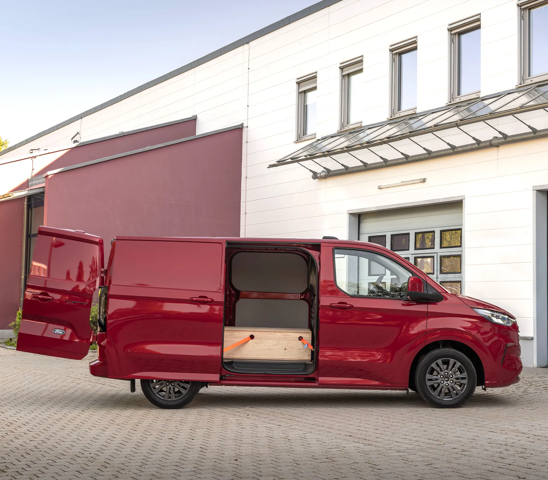Seitenansicht auf den roten Transit-Custom mit geöffneter Seiten und Hintertür und Beladung innen