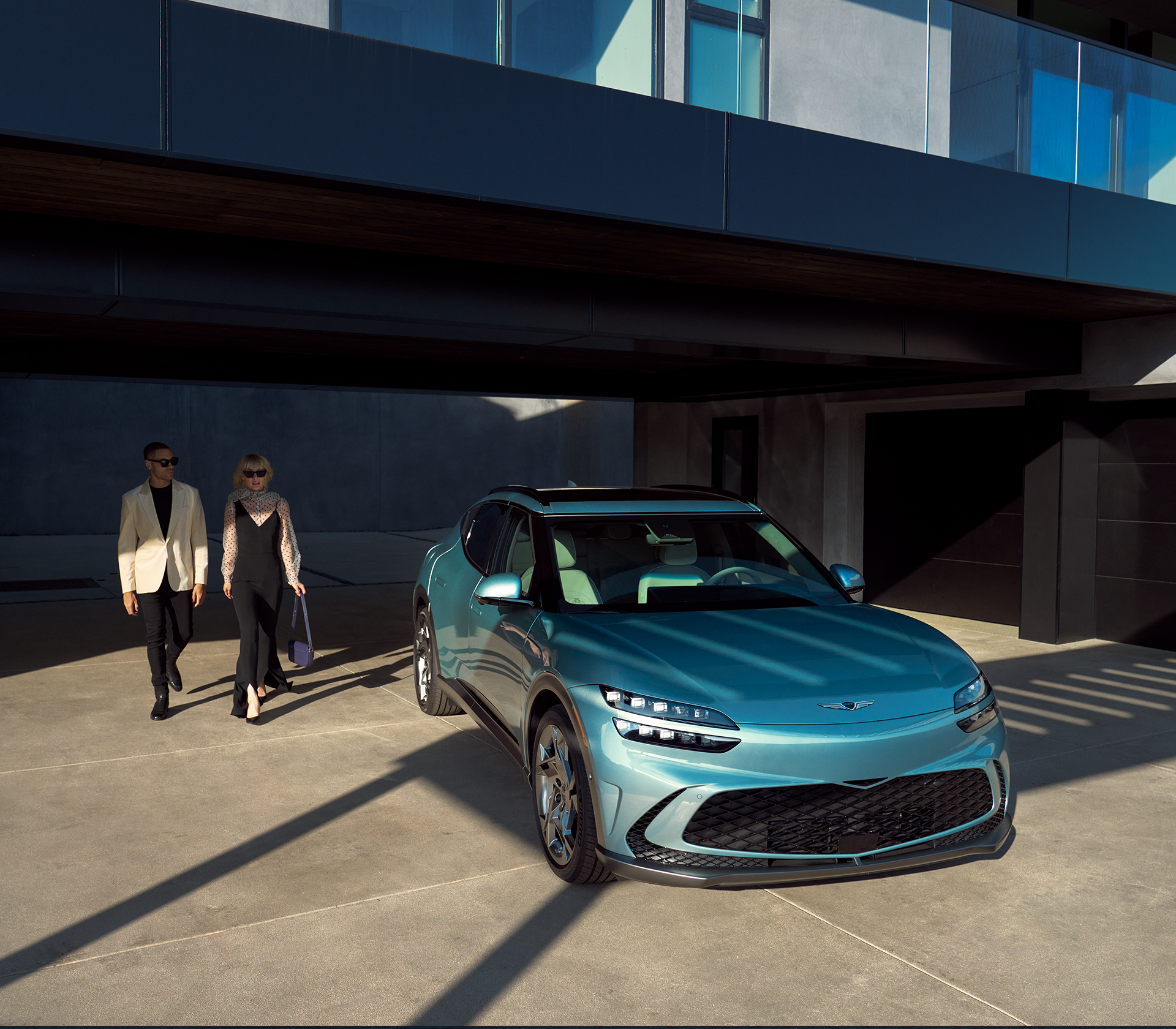 Genesis GV 60 parkt unter einer Überdachung mit zwei Menschen, die auf das Auto zulaufen
