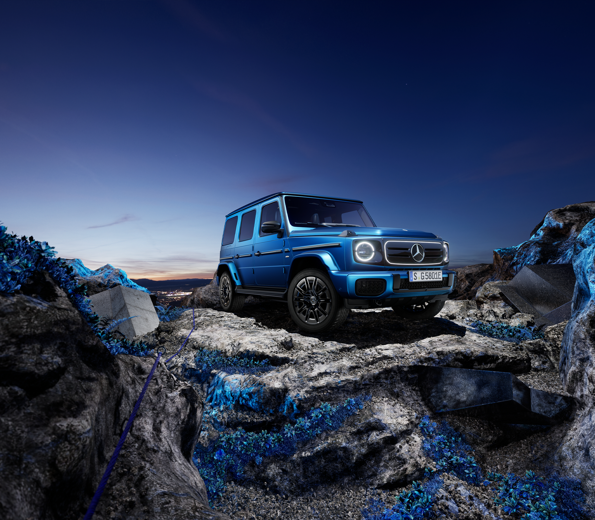 Mercedes-Benz G-Klasse elektrisch in blau steht auf einem Felsen bei Nacht mit einer Stadt unten im Hintergrund