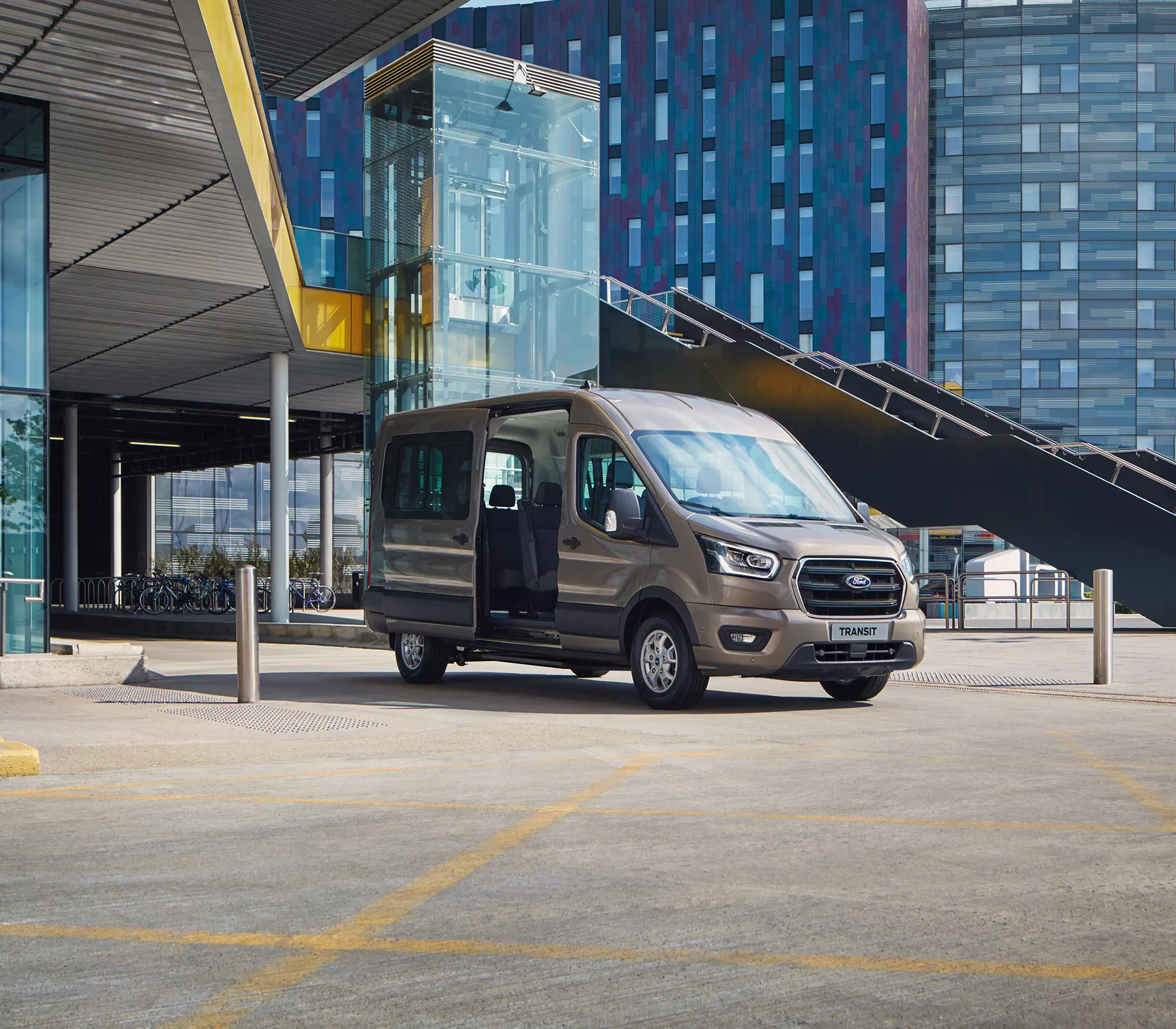 grauer Ford Transit Bus mit offener Seitentür vor Glasgebäuden