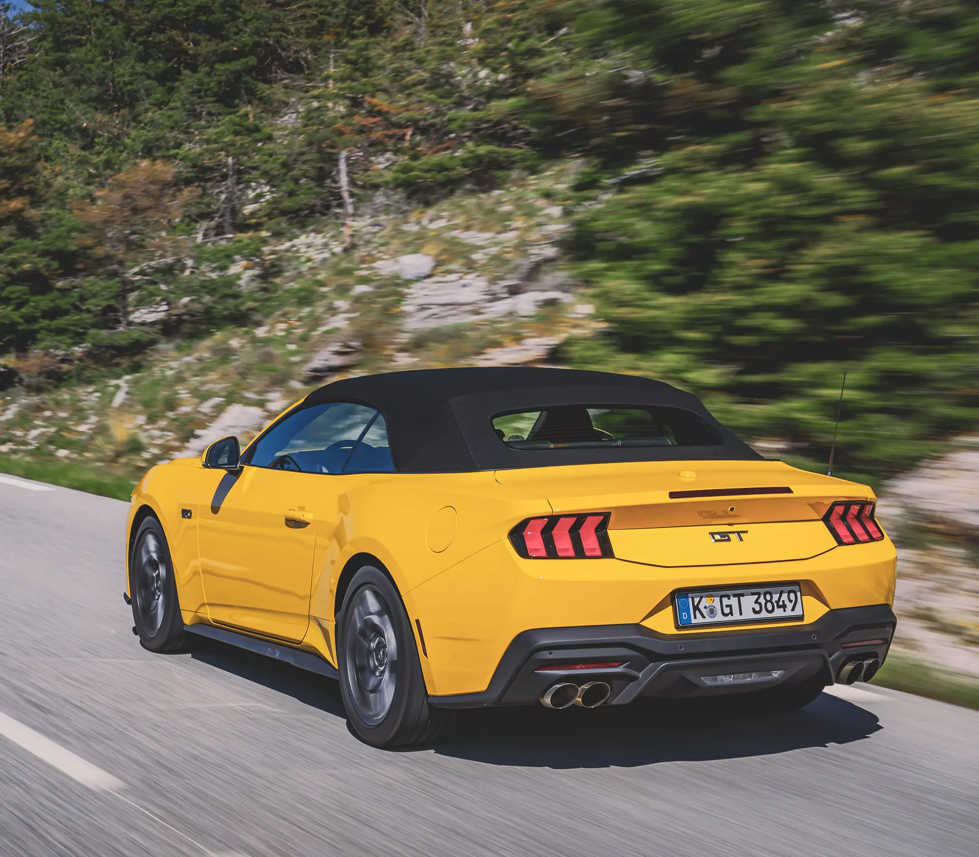 gelber Mustang fährt auf einer kurvigen Straße