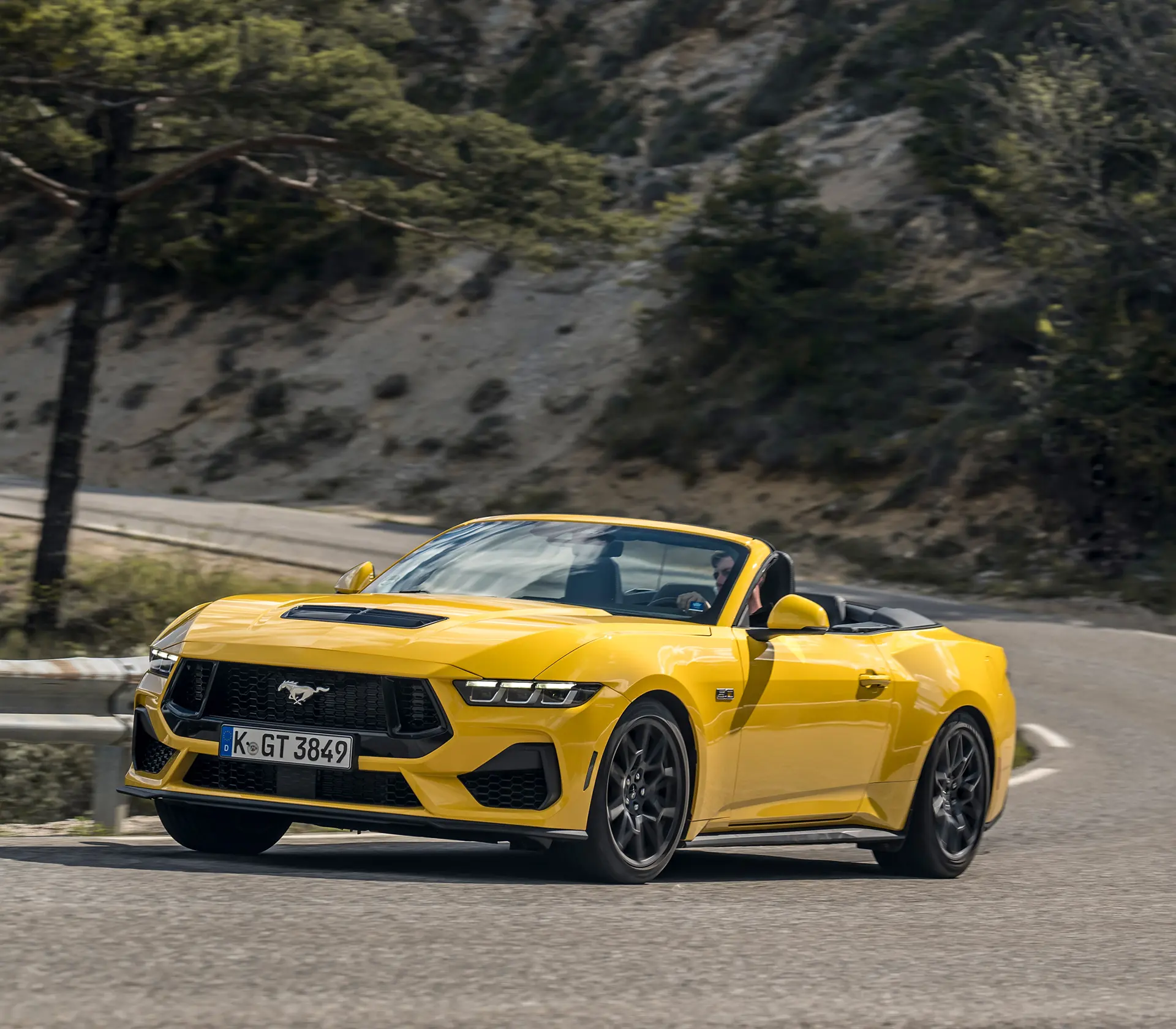 gelber Mustang als Cabrio fährt auf einer kurvigen Straße