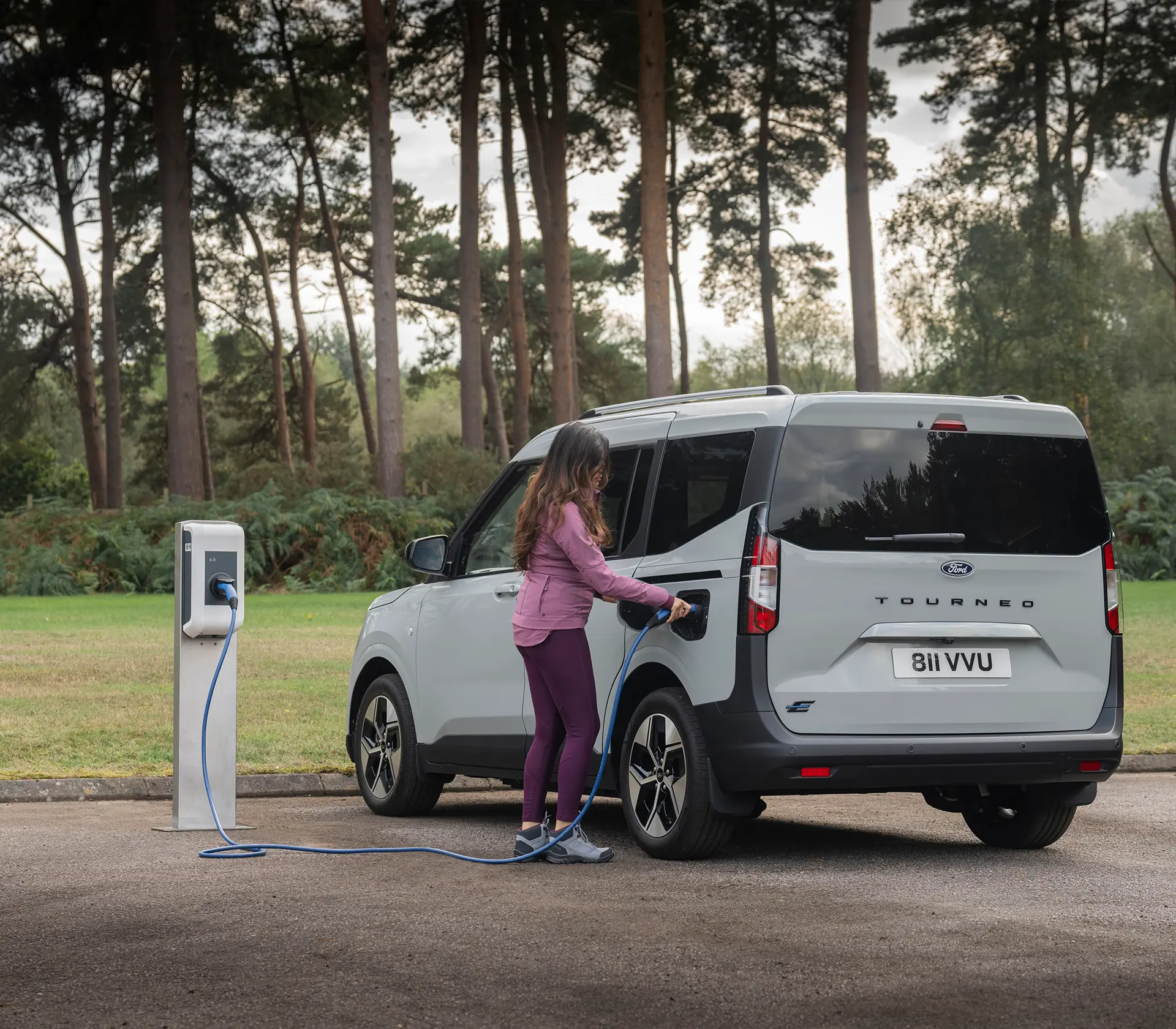 Frau läd grauen E-Tourneo Courier an der Ladesäule