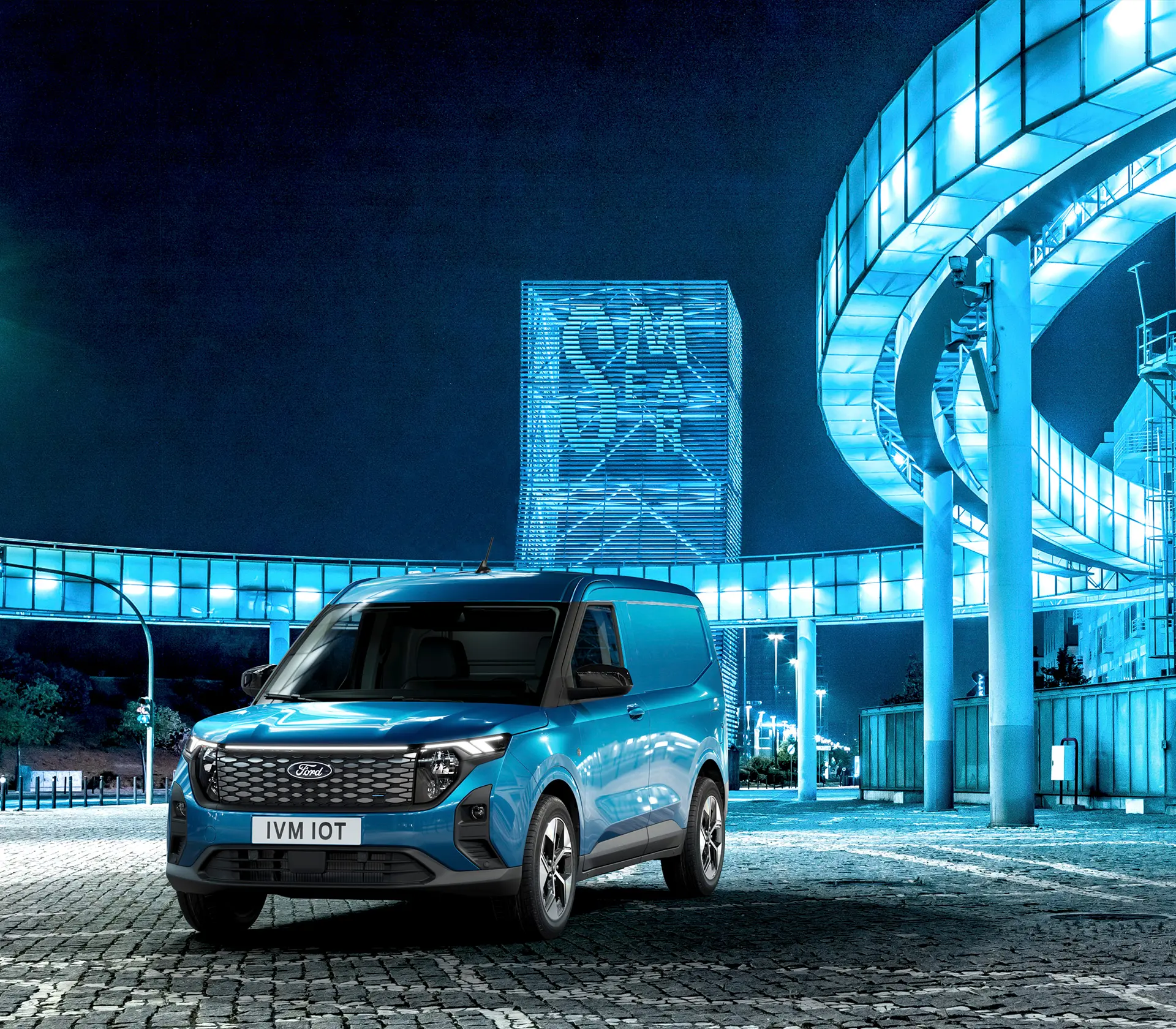 blauer E-Transit Courier bei Nacht mit Blau leuchtenden Gebäuden im Hintergrund