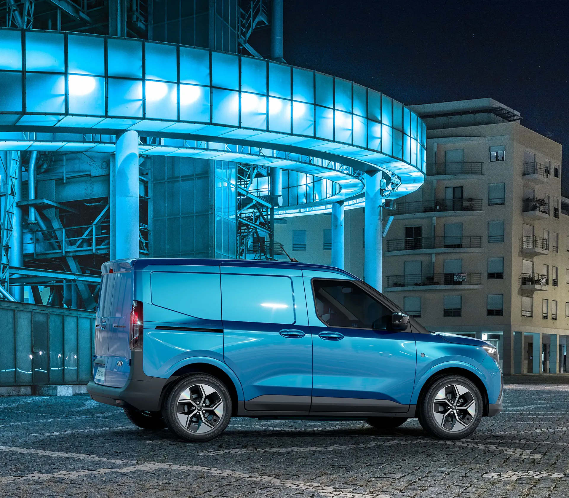 blauer E-Transit Courier bei Nacht mit Blau leuchtenden Gebäuden im Hintergrund