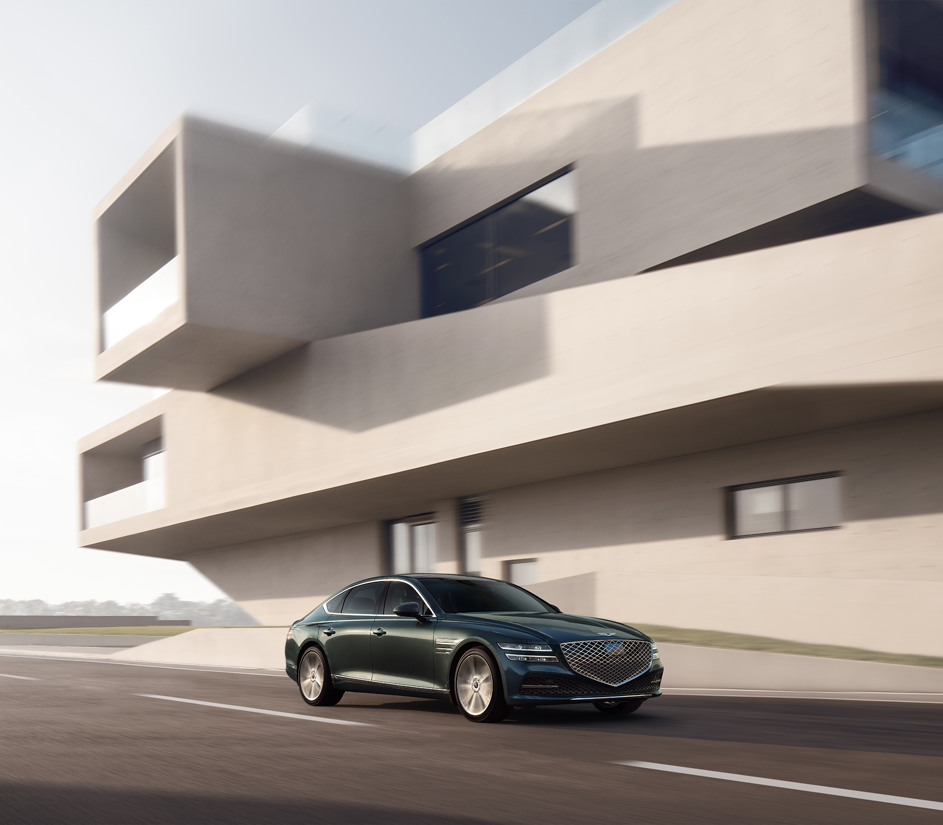 Genesis GV 801 von der Seite und Front fährt auf der Straße mit einem modernen Gebäude im Hintergrund