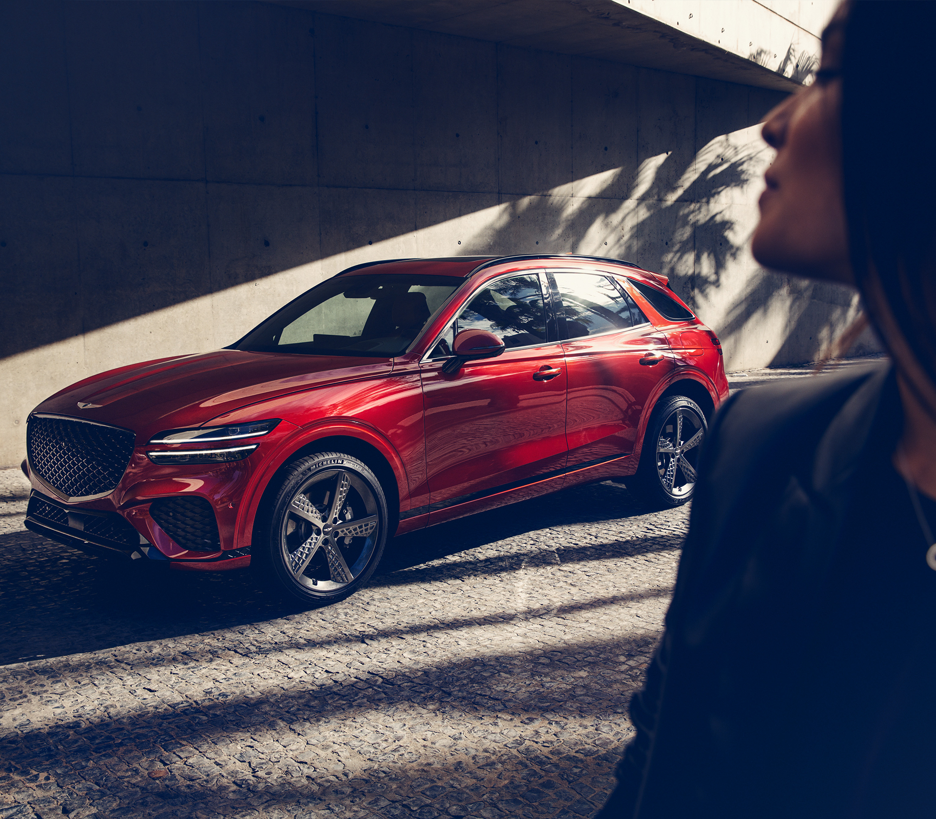Genesis GV 70 Seitenprofil einer Frau im Vordergrund. Im Hintergrund steht das Fahrzeug schräg