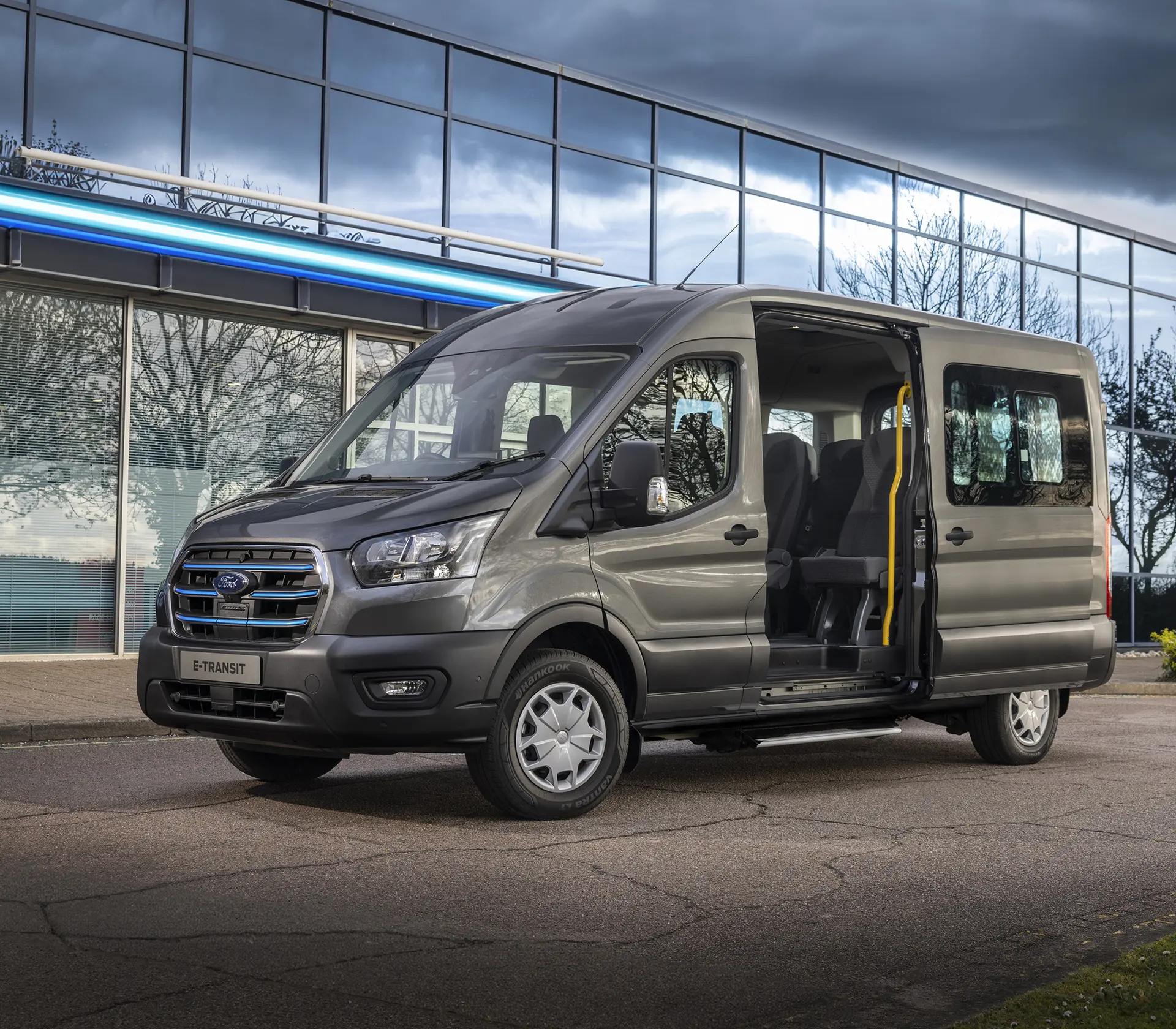 ein grauer E-Transit Bus seitlich vor einem Gebäude mit geöffneter Tür