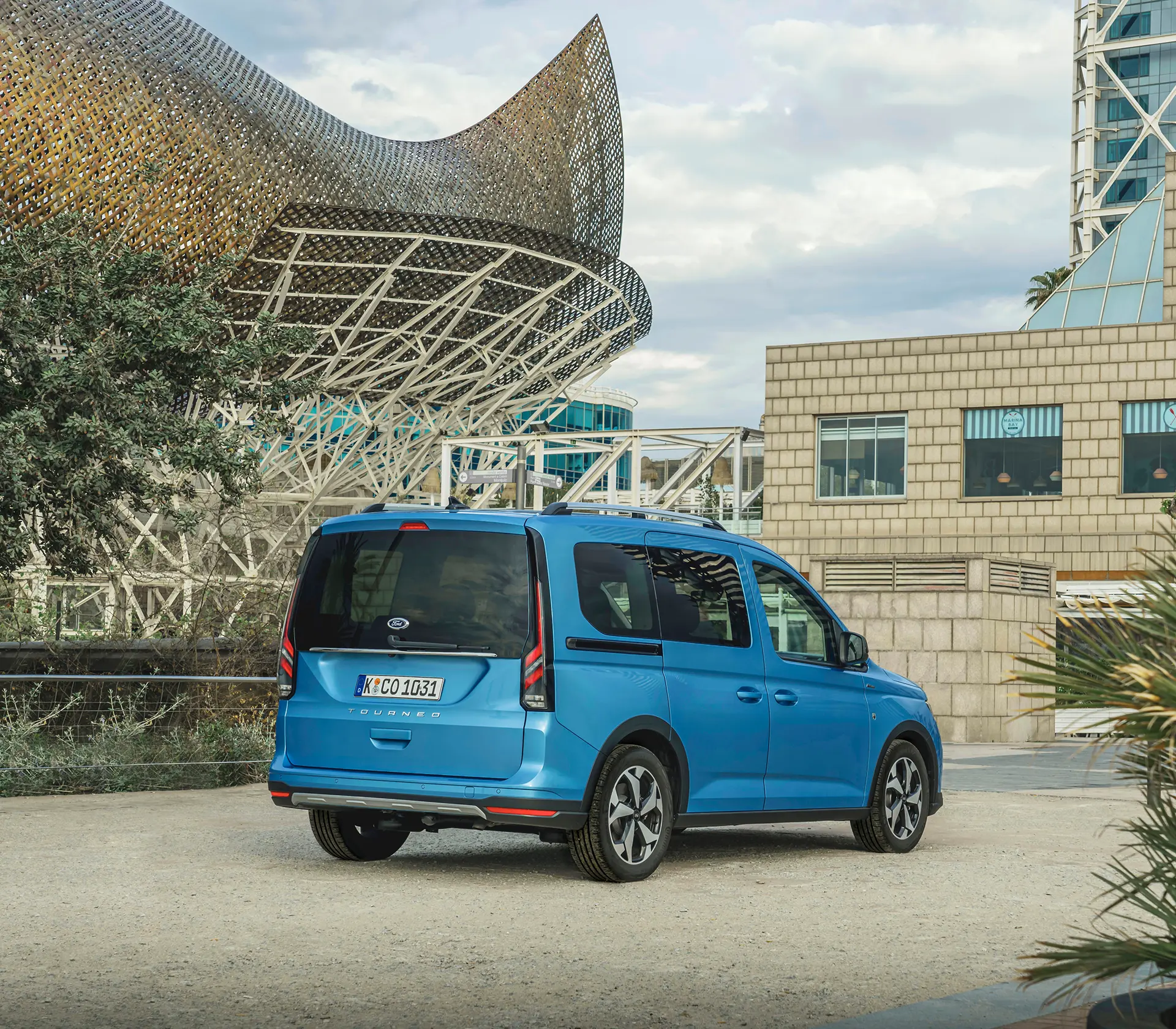 Frontansicht auf den blauen Ford Tourneo-Connect vor Bäumen und einem Gebäude