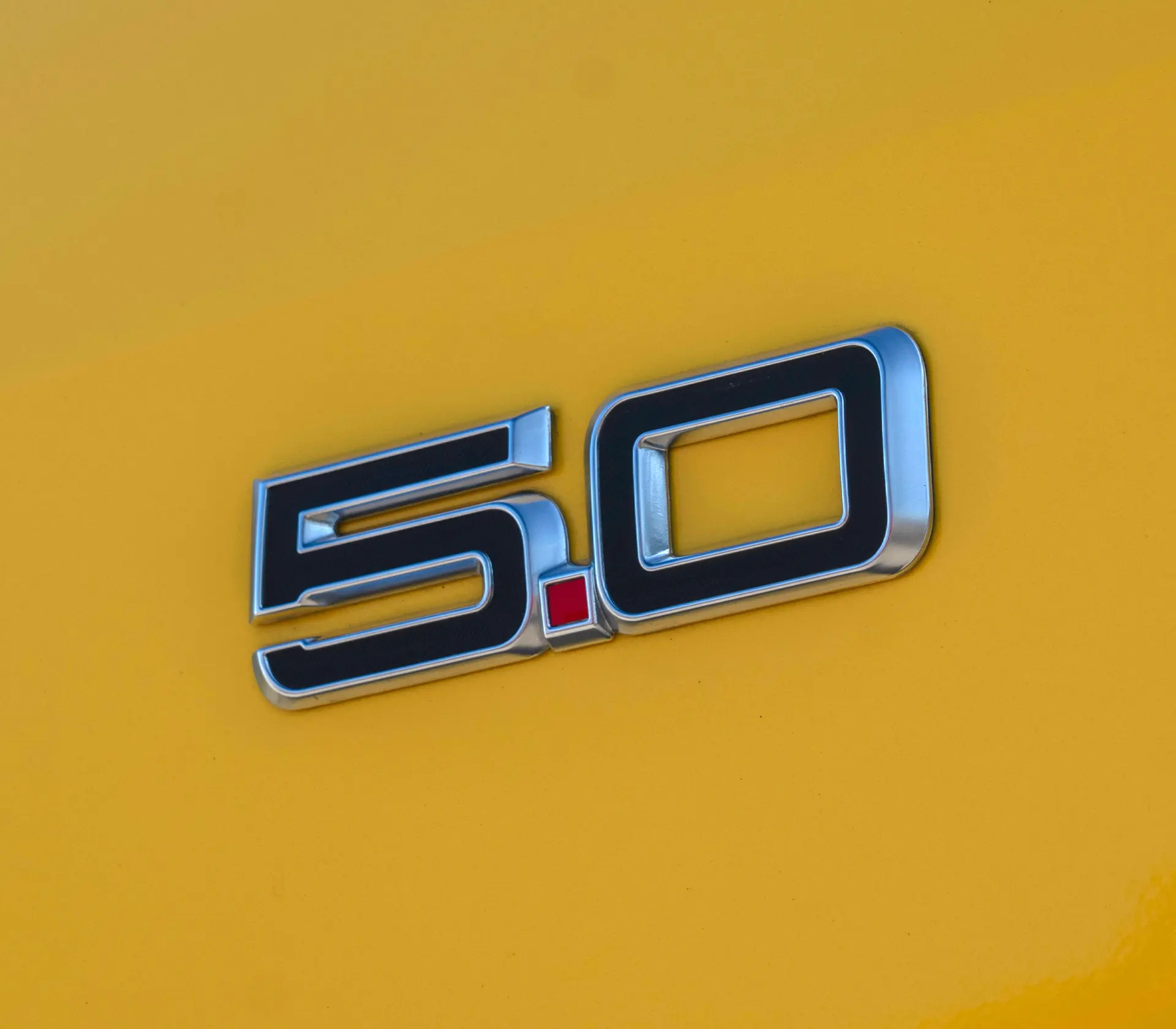 Detailaufnahme vom 5.0 Logo beim gelben Mustang