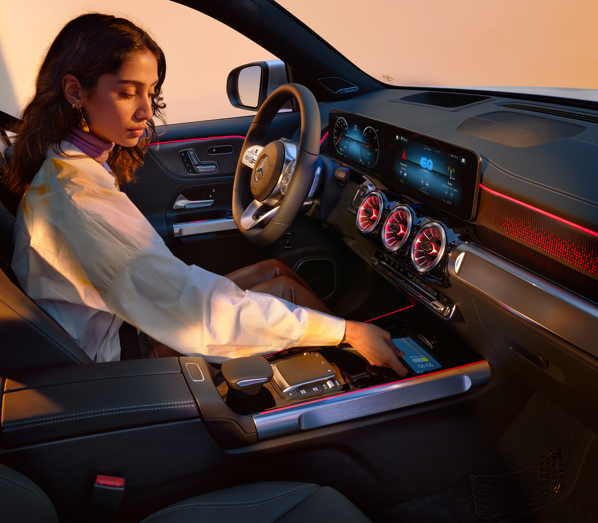 Mercedes-Benz EQB  Frau sitzt auf dem Fahrersitzt und tut ihr Handy in die Kabellose Ladestation im Auto