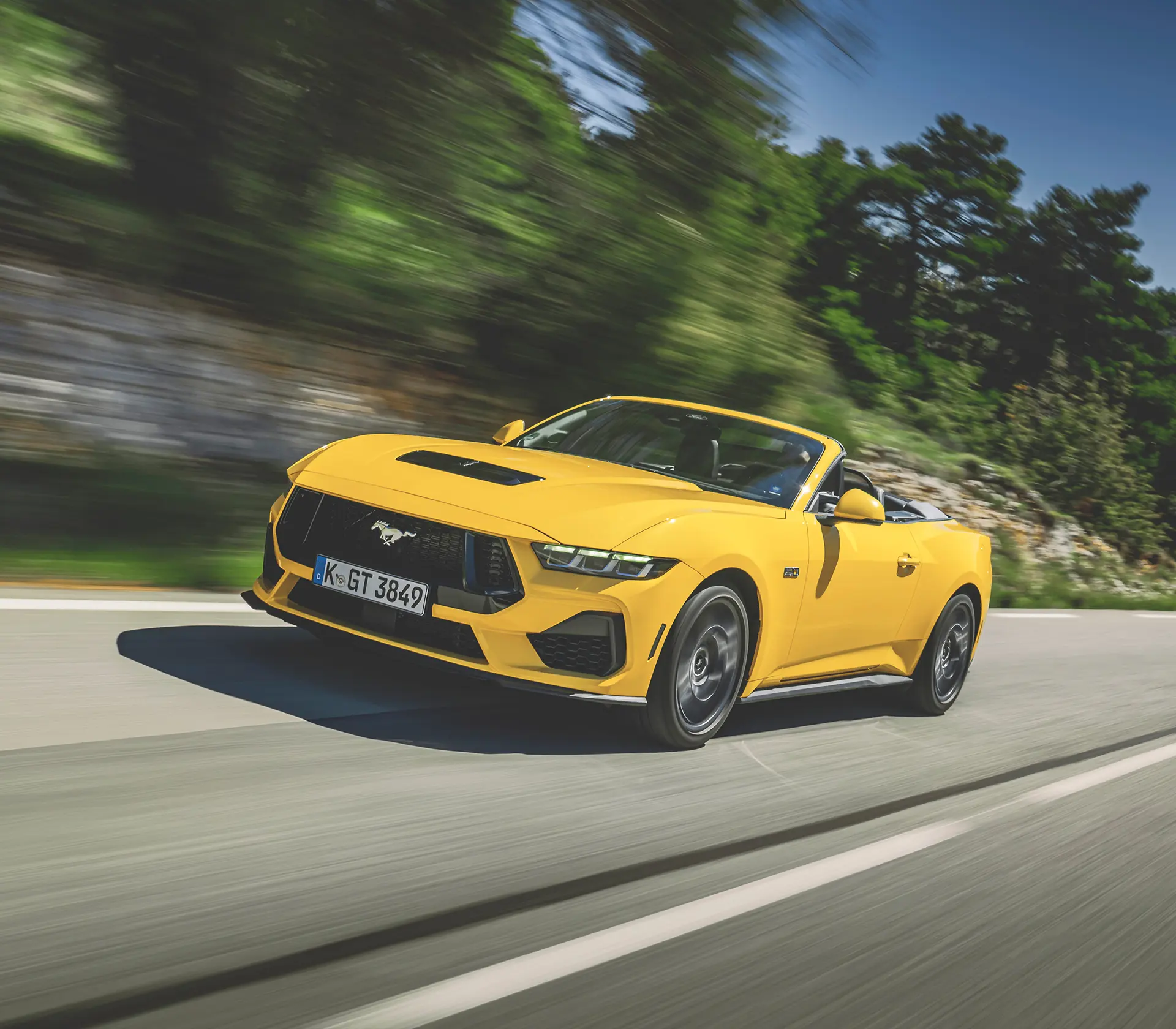 gelber Mustang als Cabrio fährt auf einer kurvigen Straße