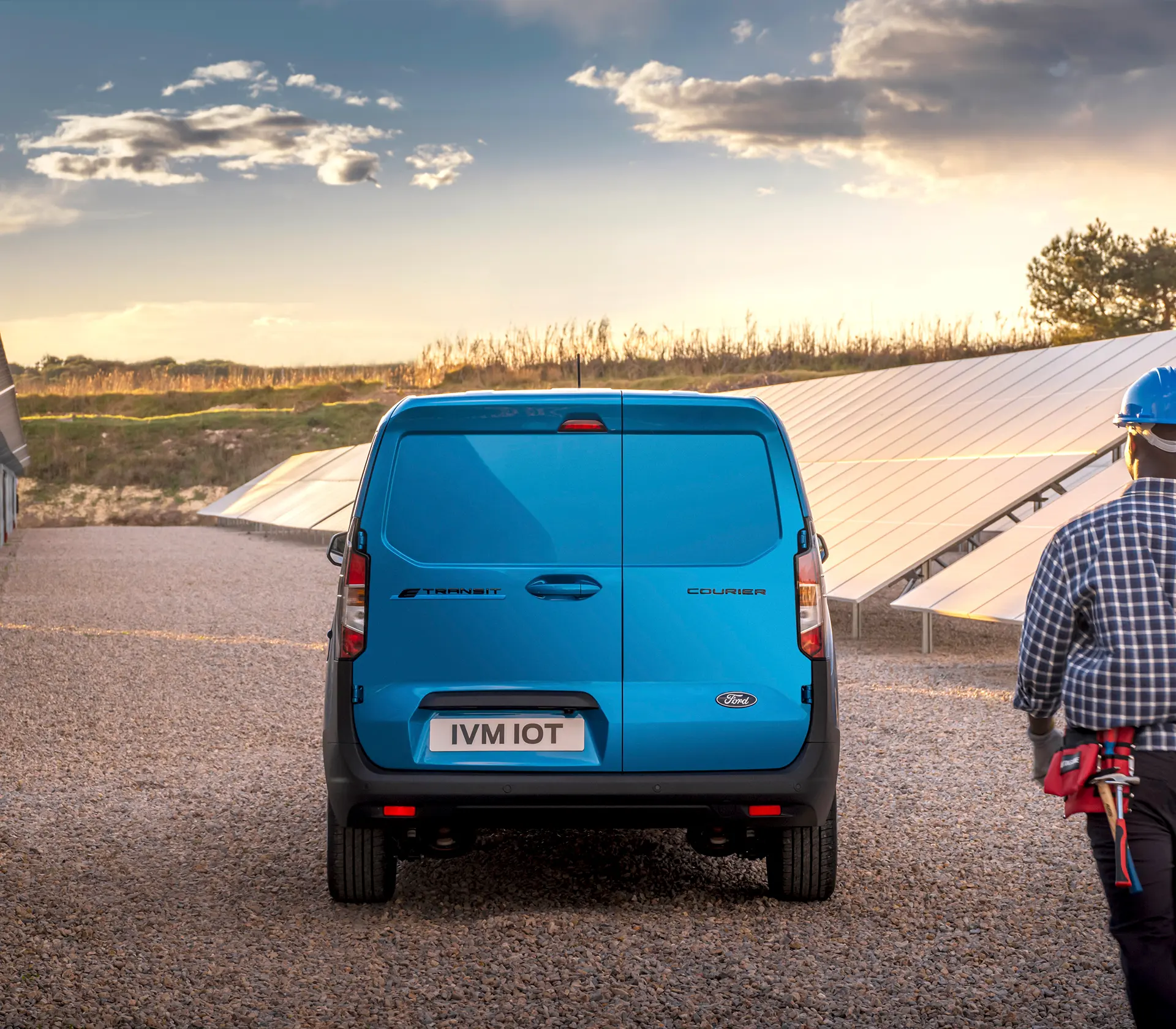 blauer E-Transit Courier im Sonnenuntergang - Arbeiter läuft auf das Fahrzeug zu