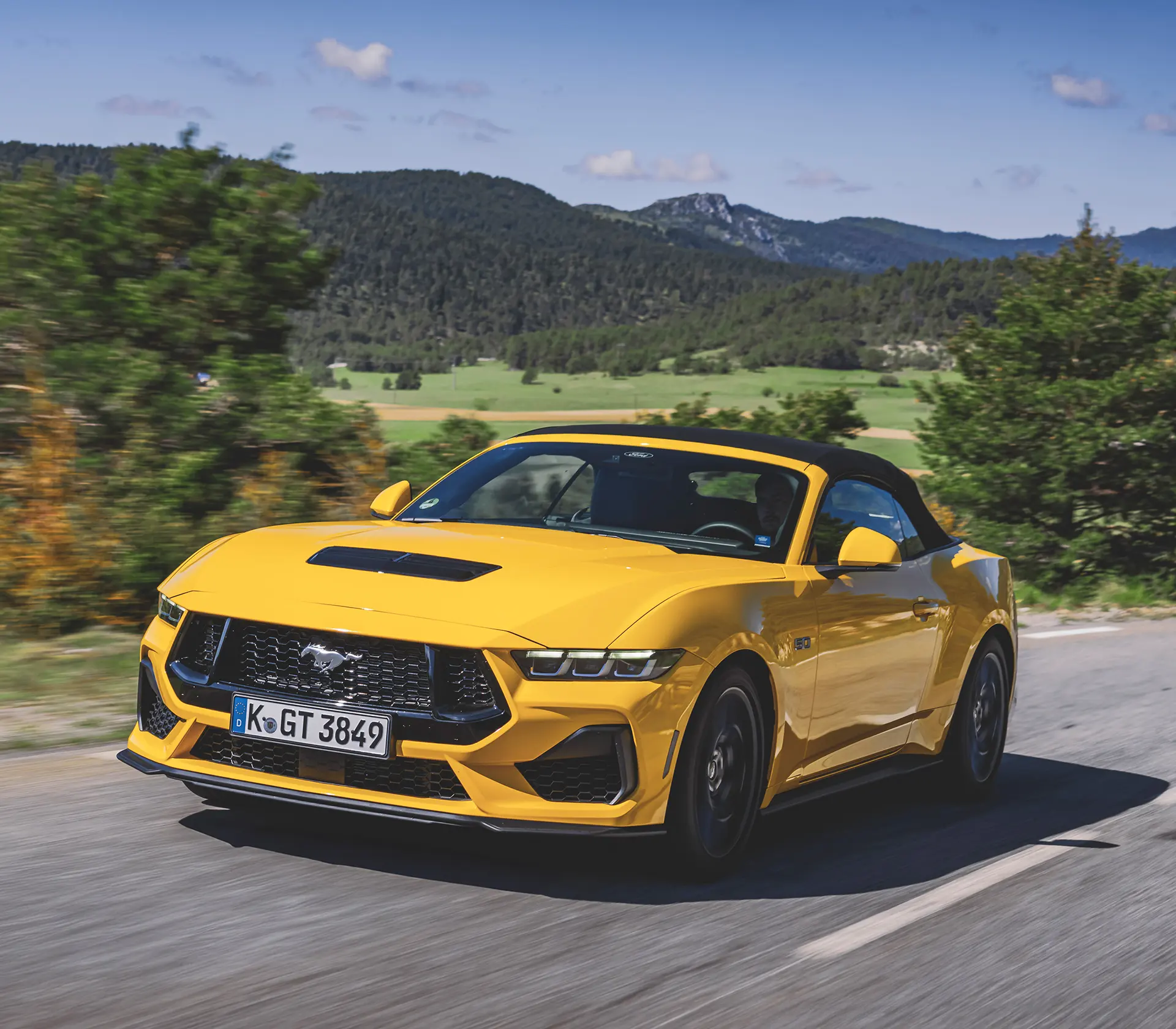 gelber Mustang fährt auf einer kurvigen Straße