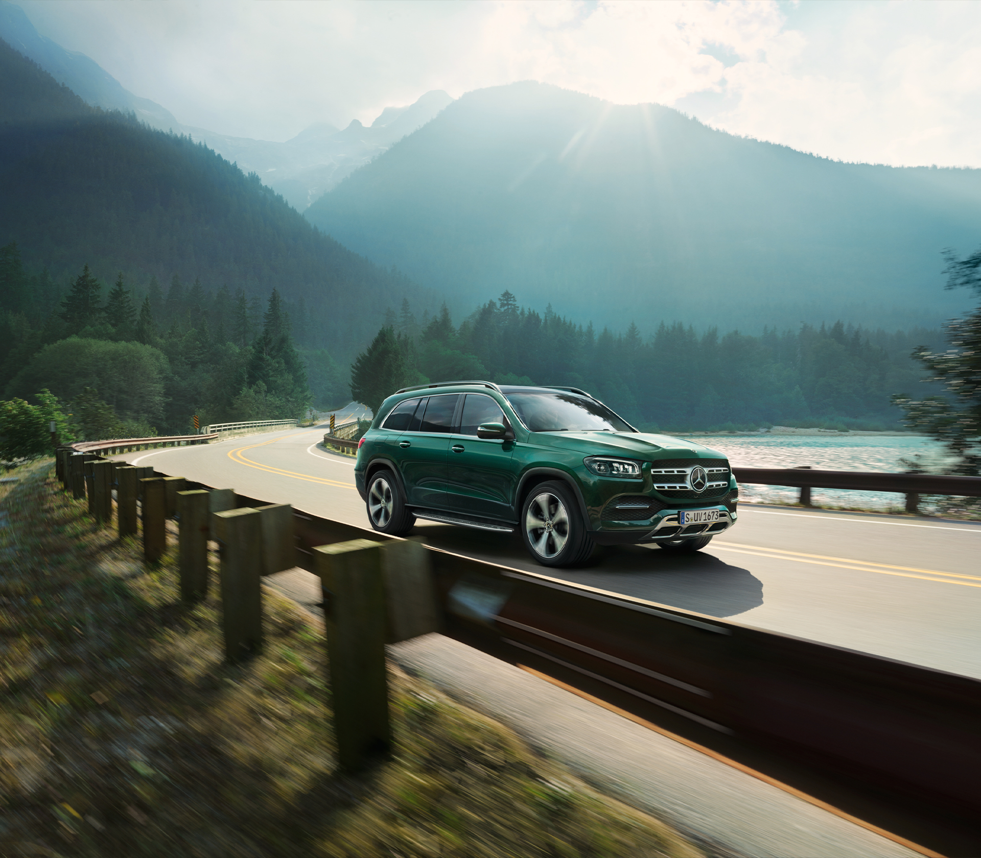 Mercedes-Benz GLS fährt auf einer Landstraße mit Bergen und der Sonne im Hintergrund. Ansicht von der Seite 