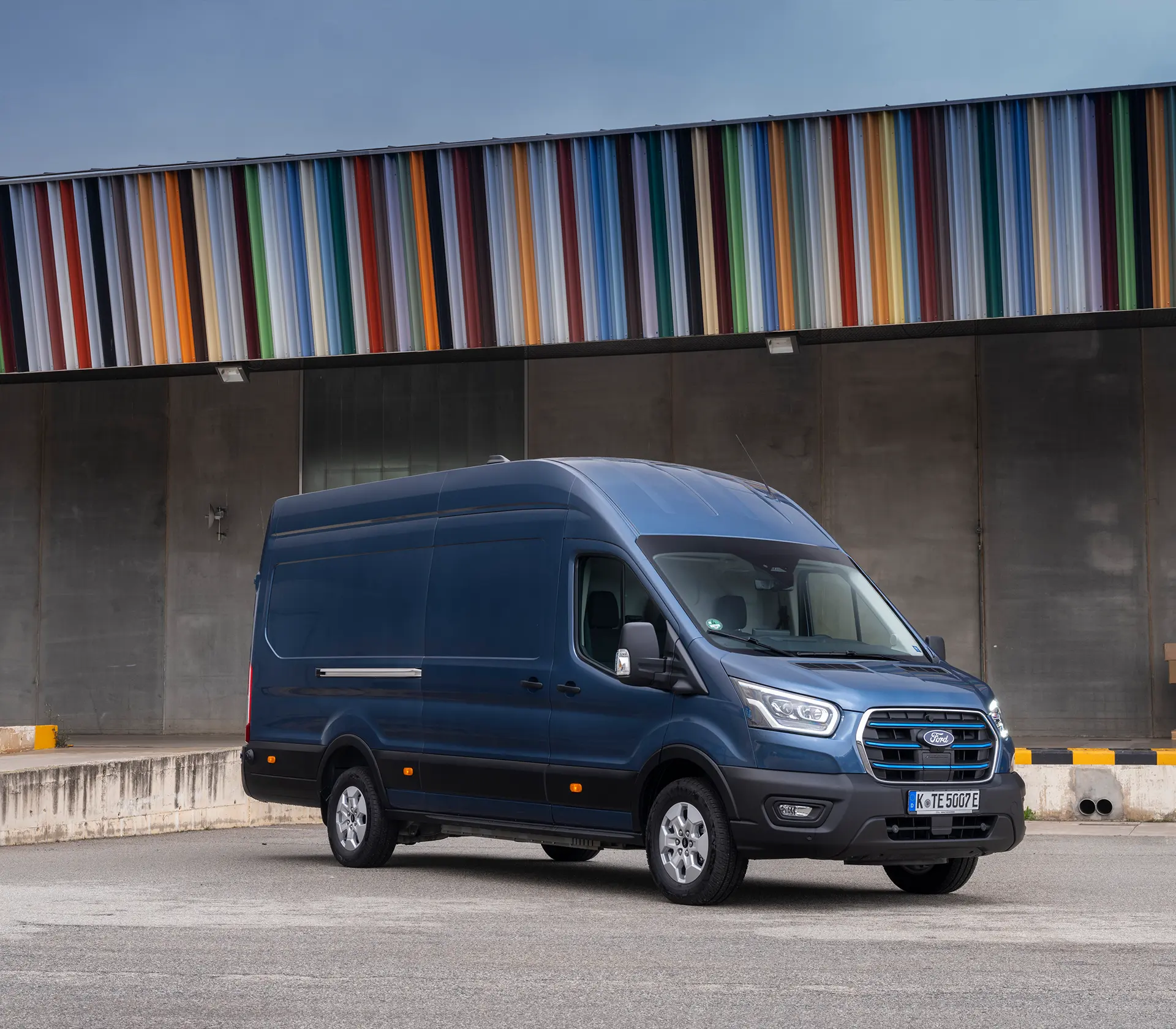 blauer E-Transit steht seitlich mit Bunten Dach im Hintergrund