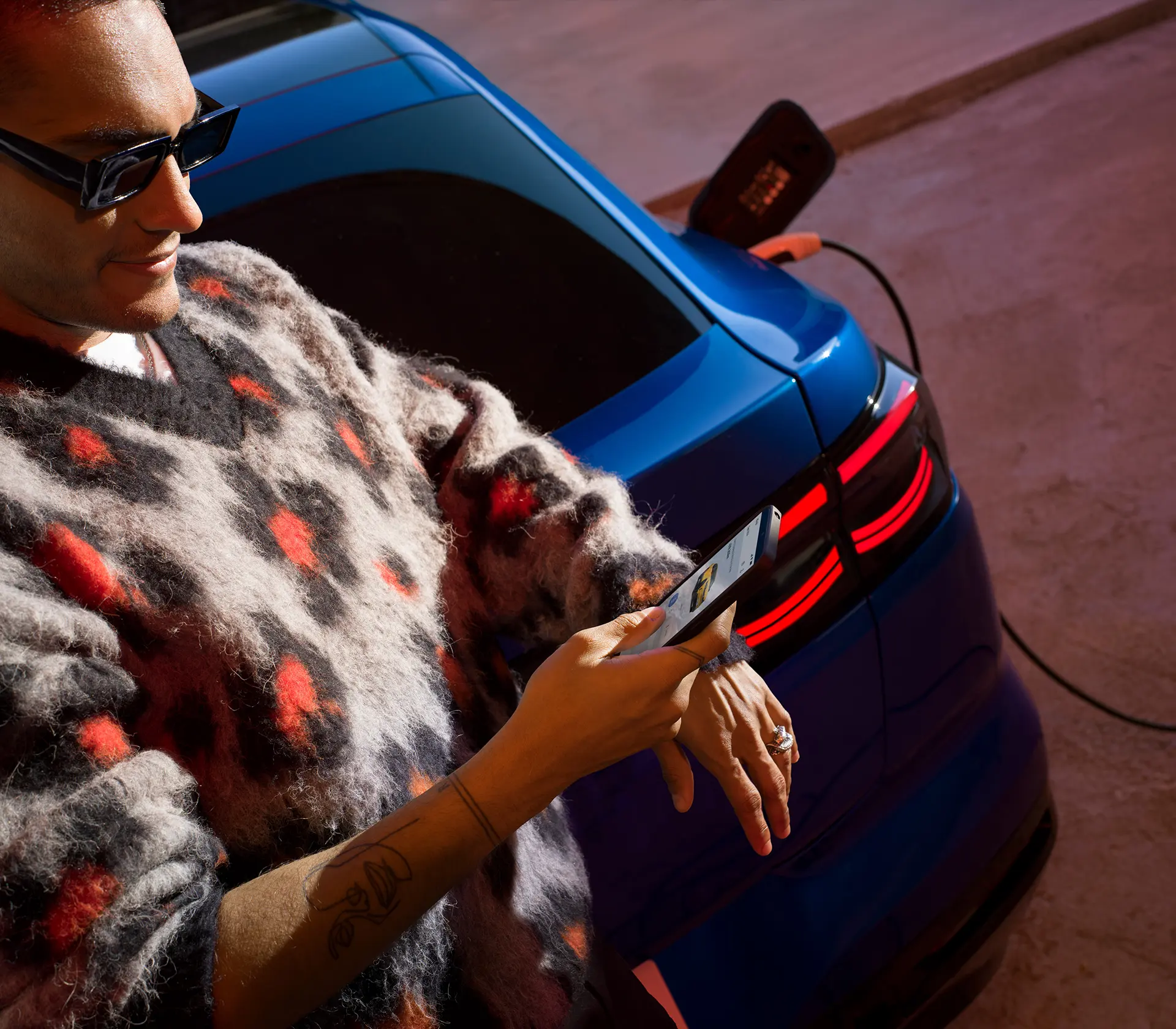 Mann schaut auf sein Handy während im Hintergrund ein blauer Capri am Laden ist