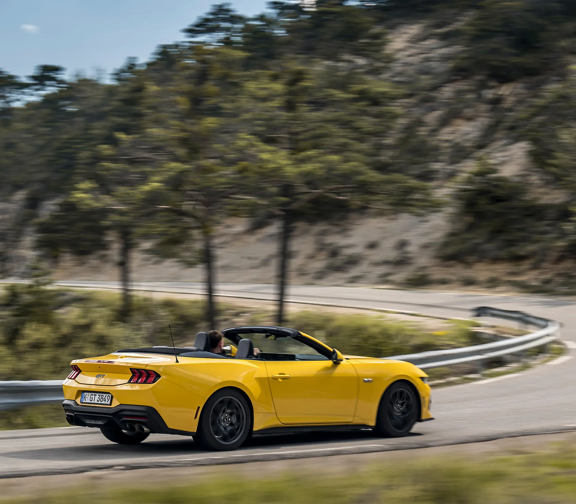 gelber Mustang als Cabrio fährt auf einer kurvigen Straße