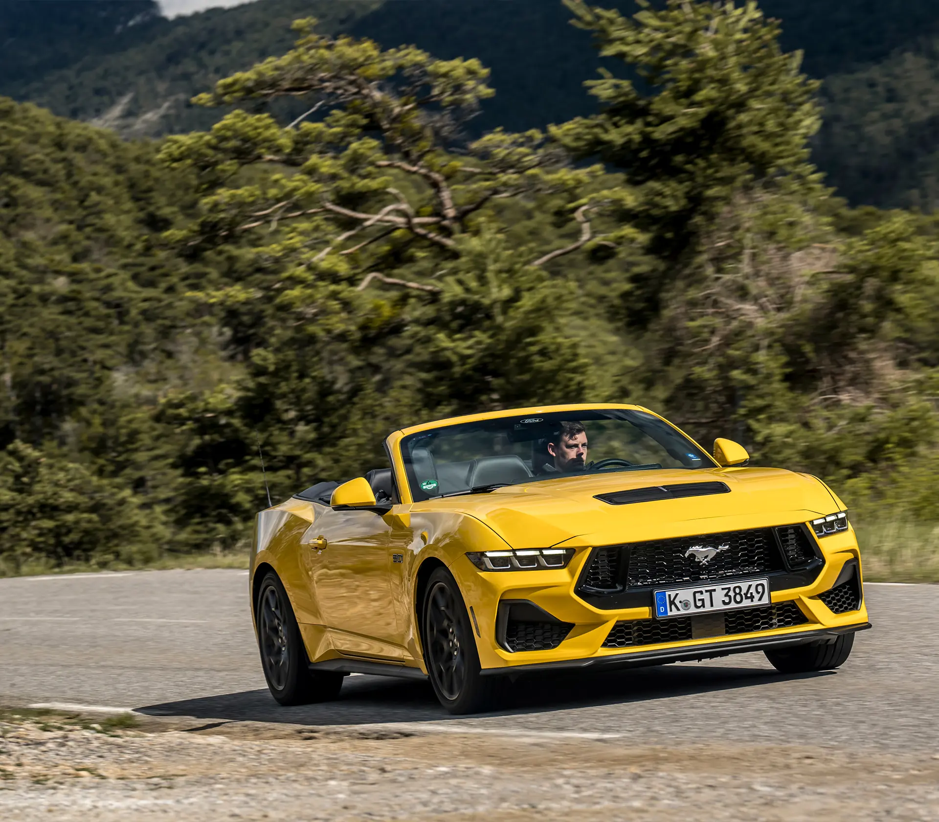 gelber Mustang als Cabrio fährt auf einer kurvigen Straße