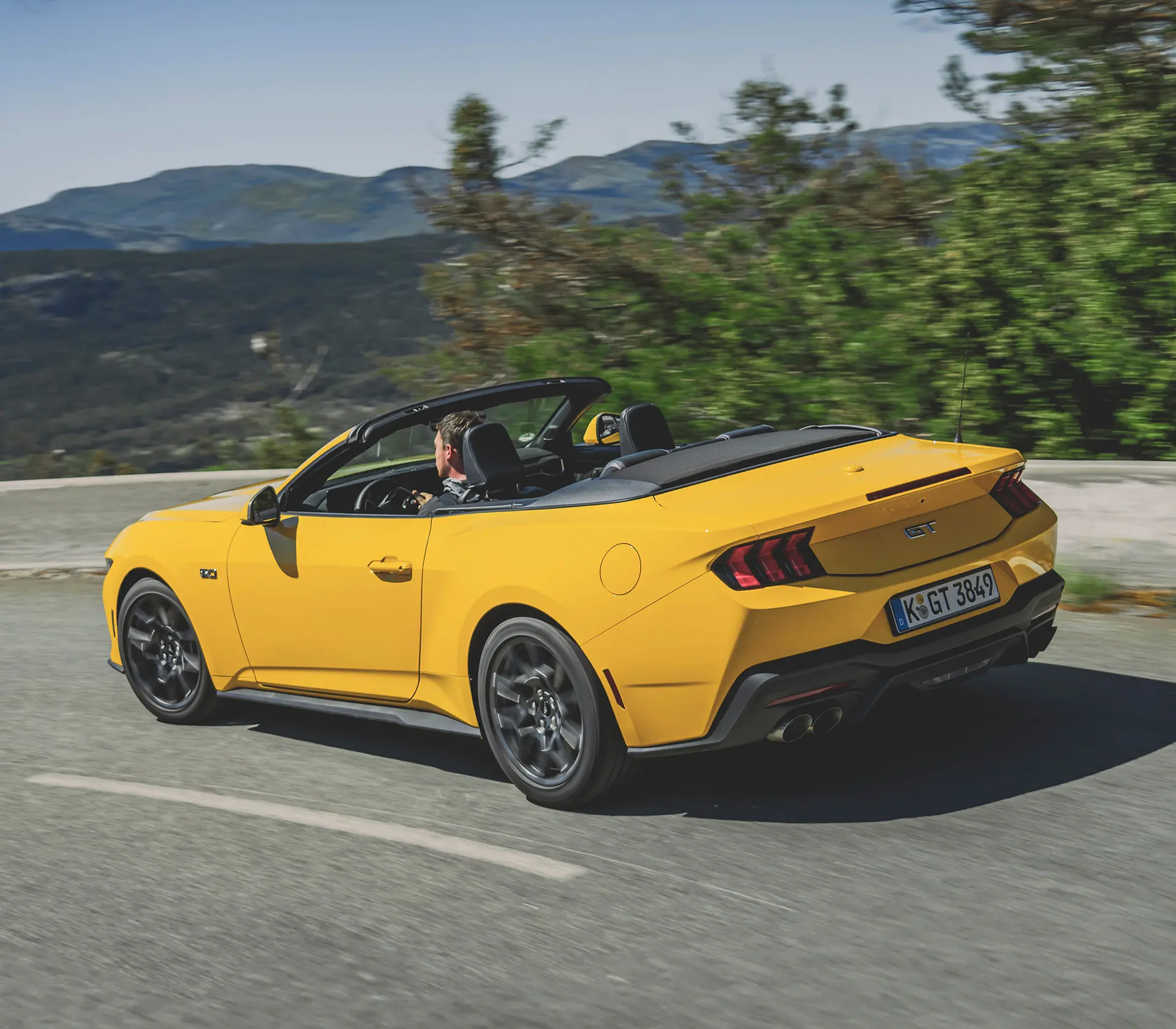 Heckansicht auf gelber Mustang als Cabrio fährt auf einer kurvigen Straße