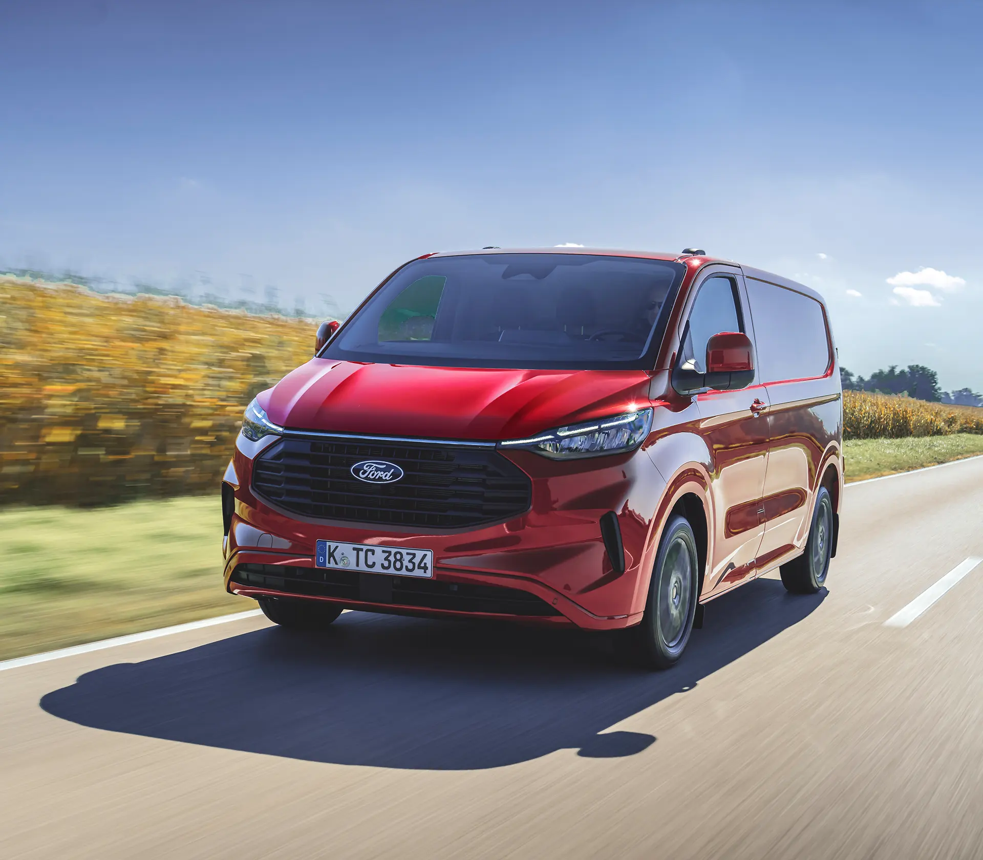 Frontansicht auf den roten Transit Custom, der auf einer Landstraße fährt