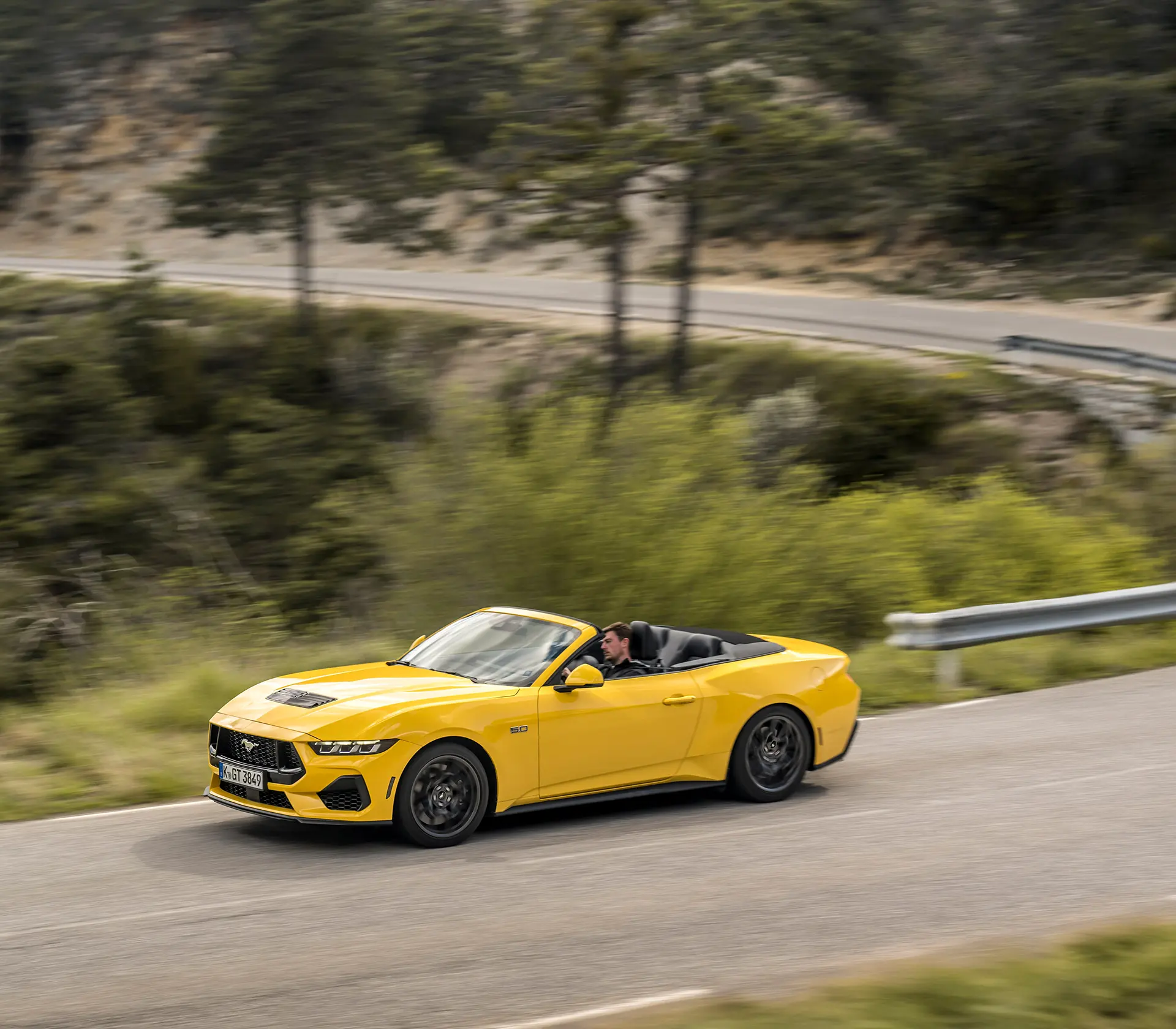 gelber Mustang als Cabrio fährt auf einer kurvigen Straße