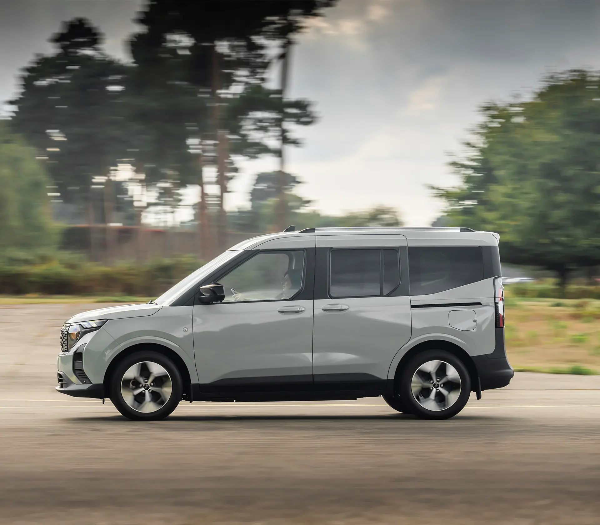Grauer E-Tourneo Courier fährt auf der Straße mit Gebirgen im Hintergrund