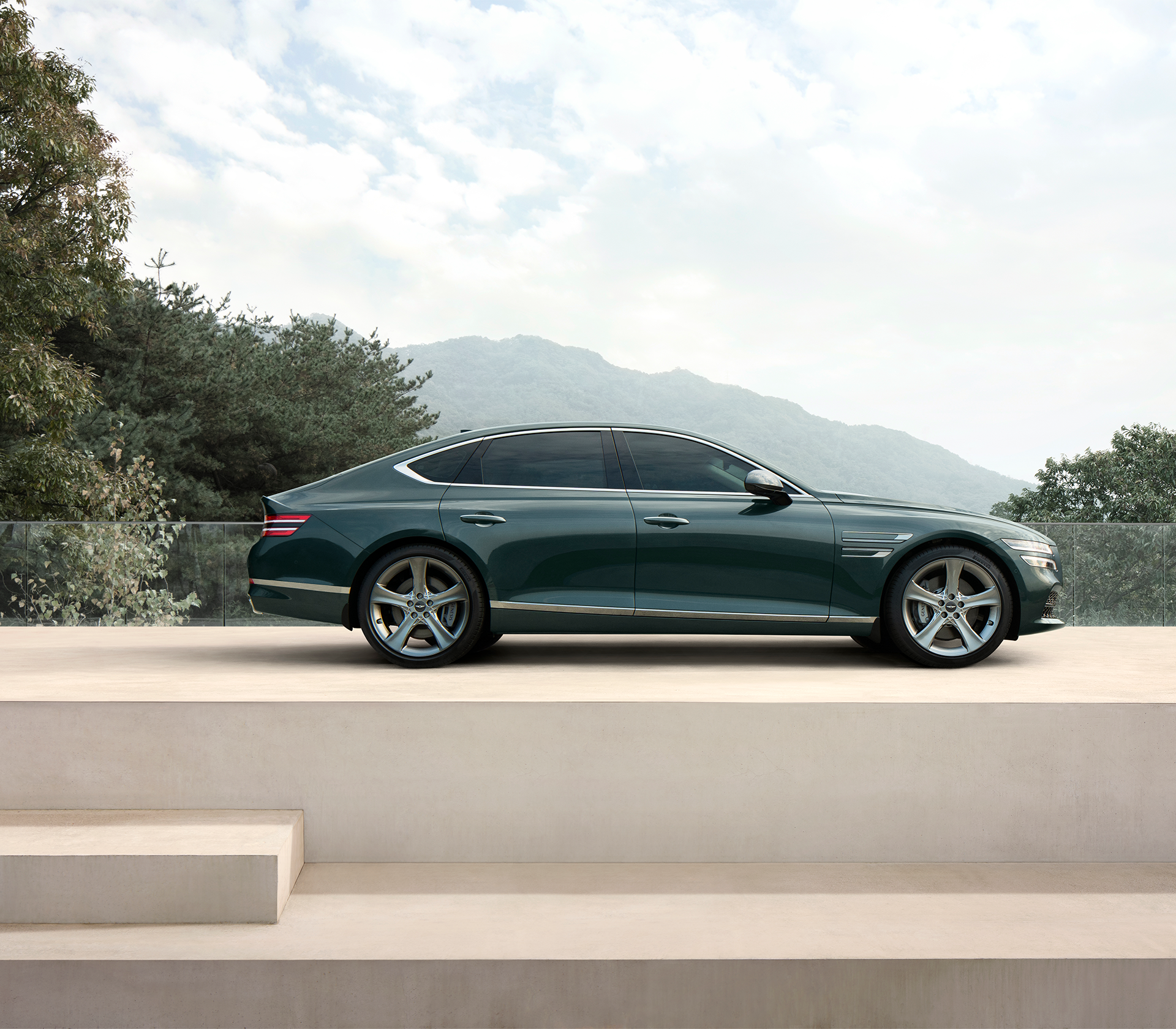 Genesis G80 von der Seite ist geparkt auf einer weißen Erhöhung mit Bergen und Wald im Hintergrund