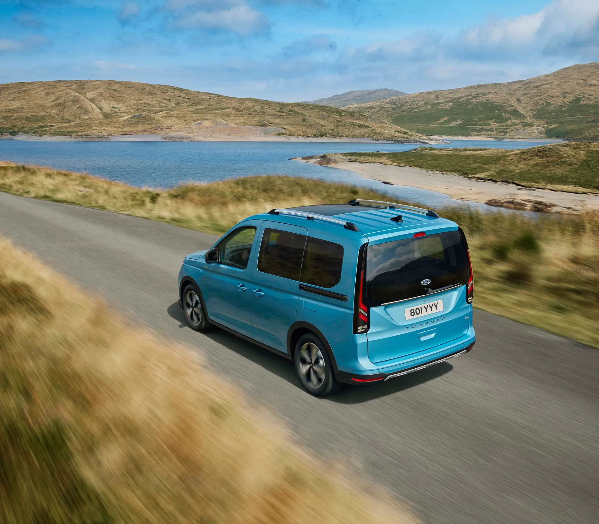 blauer Ford Tourneo-Connect fährt auf der Straße mit dem Meer im Hintergrund