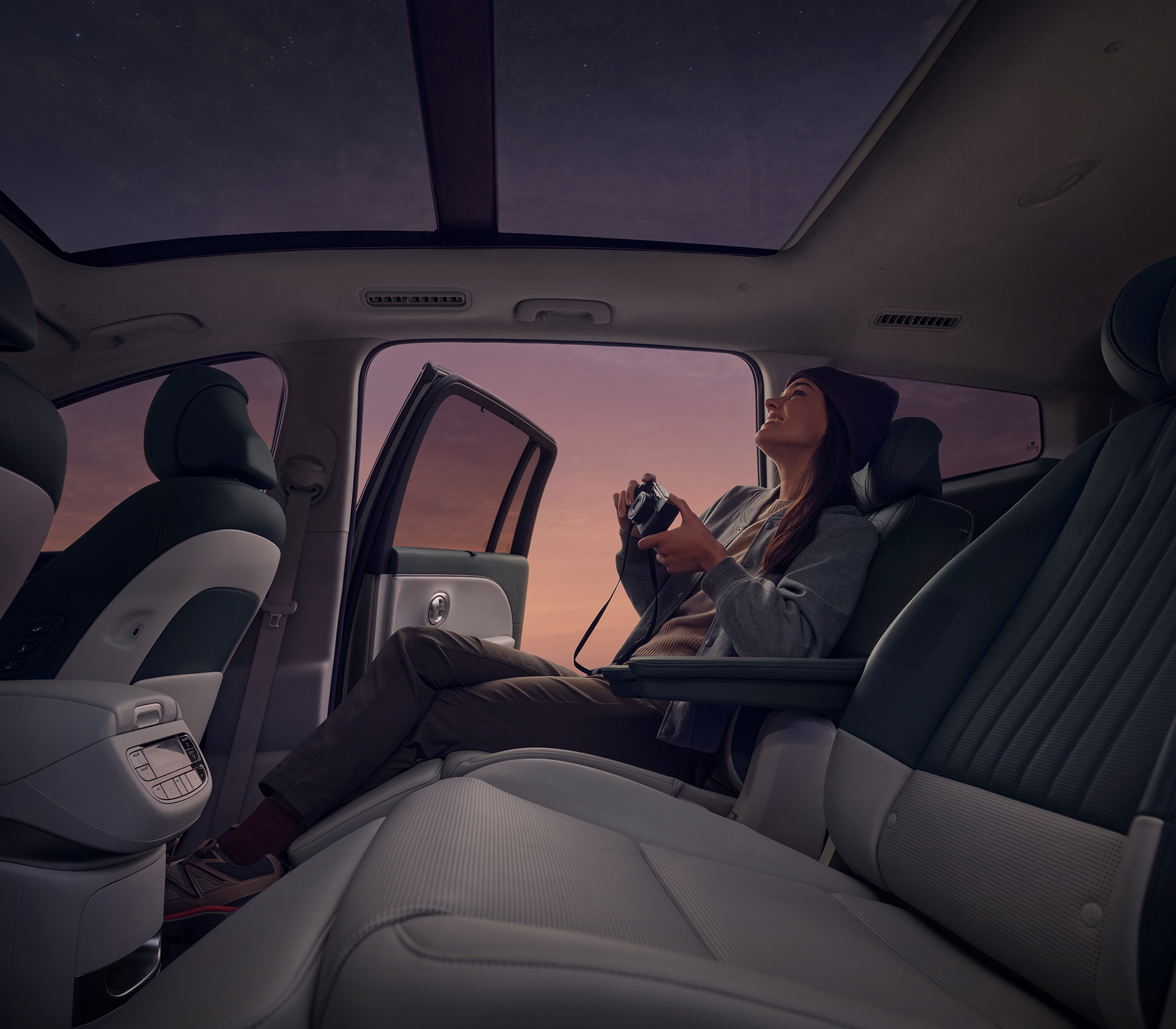 Hyundai IONIQ 9 Innenansichder Sitze und eine Frau, die bei Nacht durch das Panoramadach in die Sterne guckt und eine Kamera in der Hand hält
