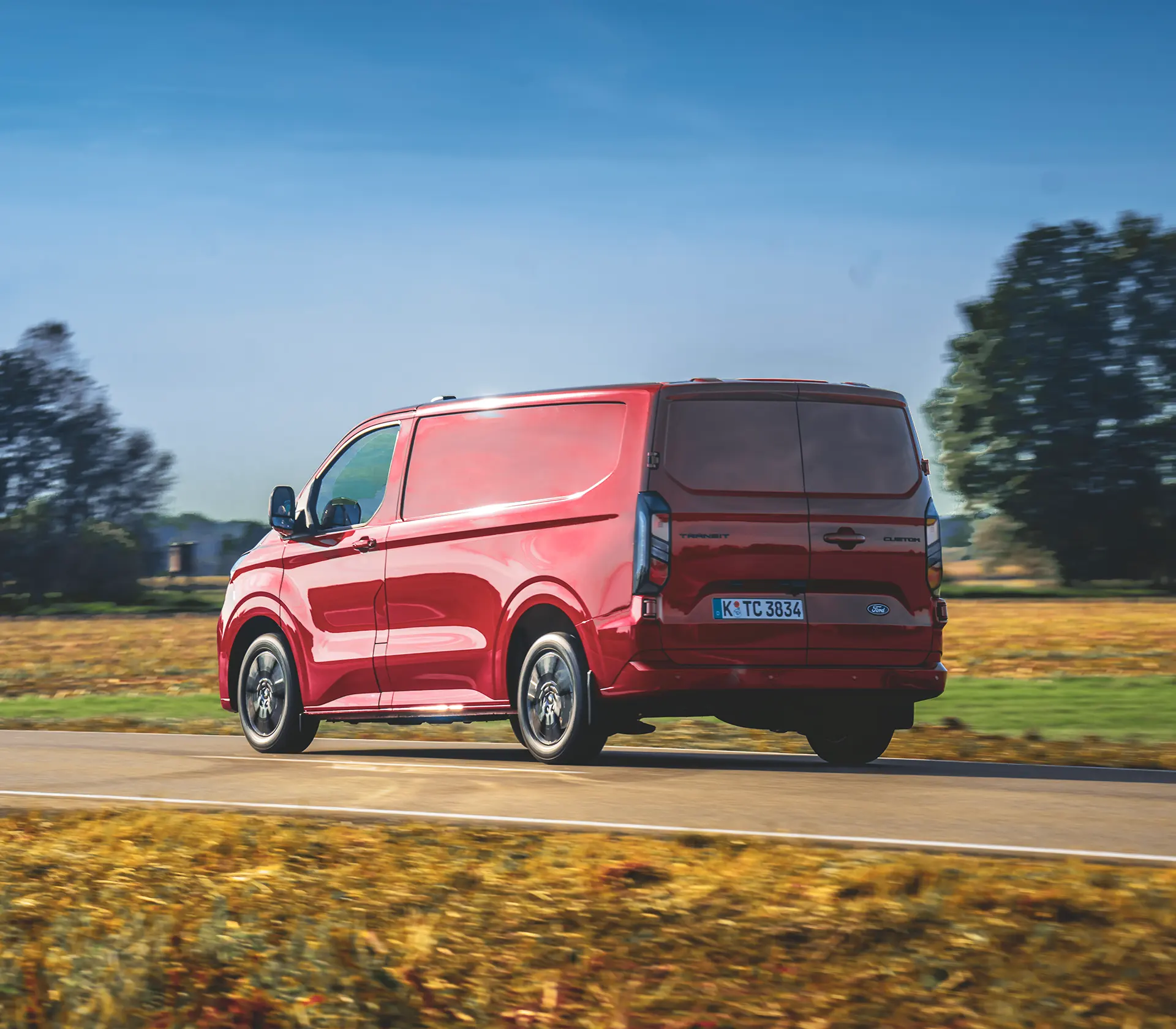 Heckansicht auf den roten Transit Custom, der auf einer Landstraße fährt