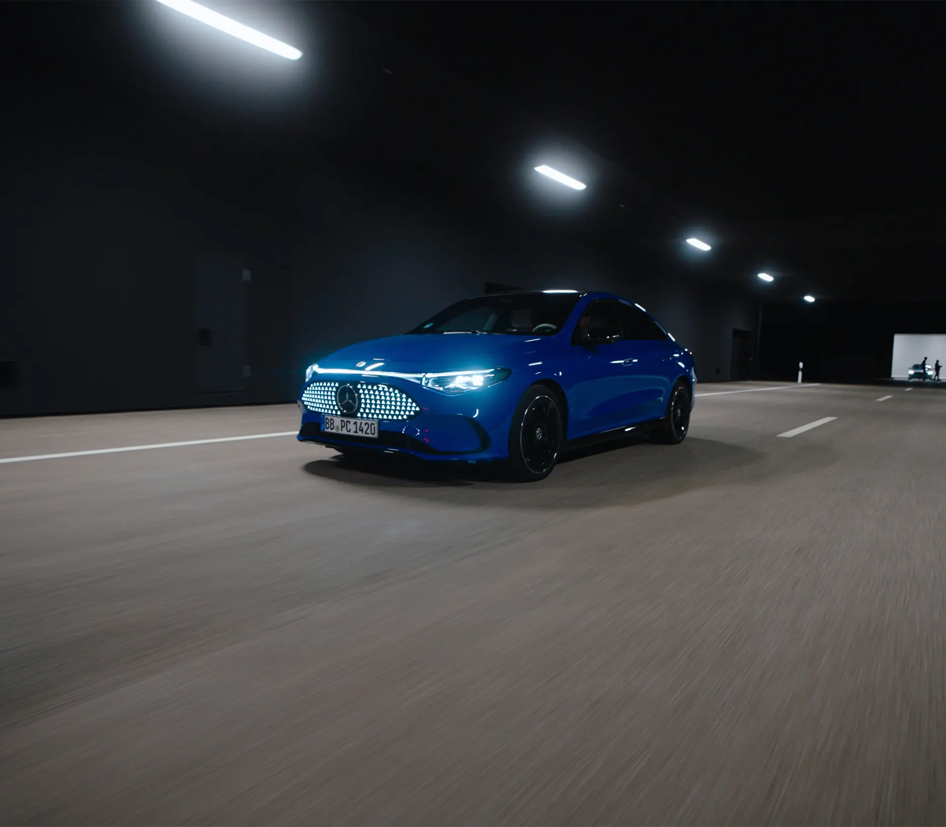 blauer Cla fährt auf der Straße, Licher und Kühlergrill sind hell am leuchten