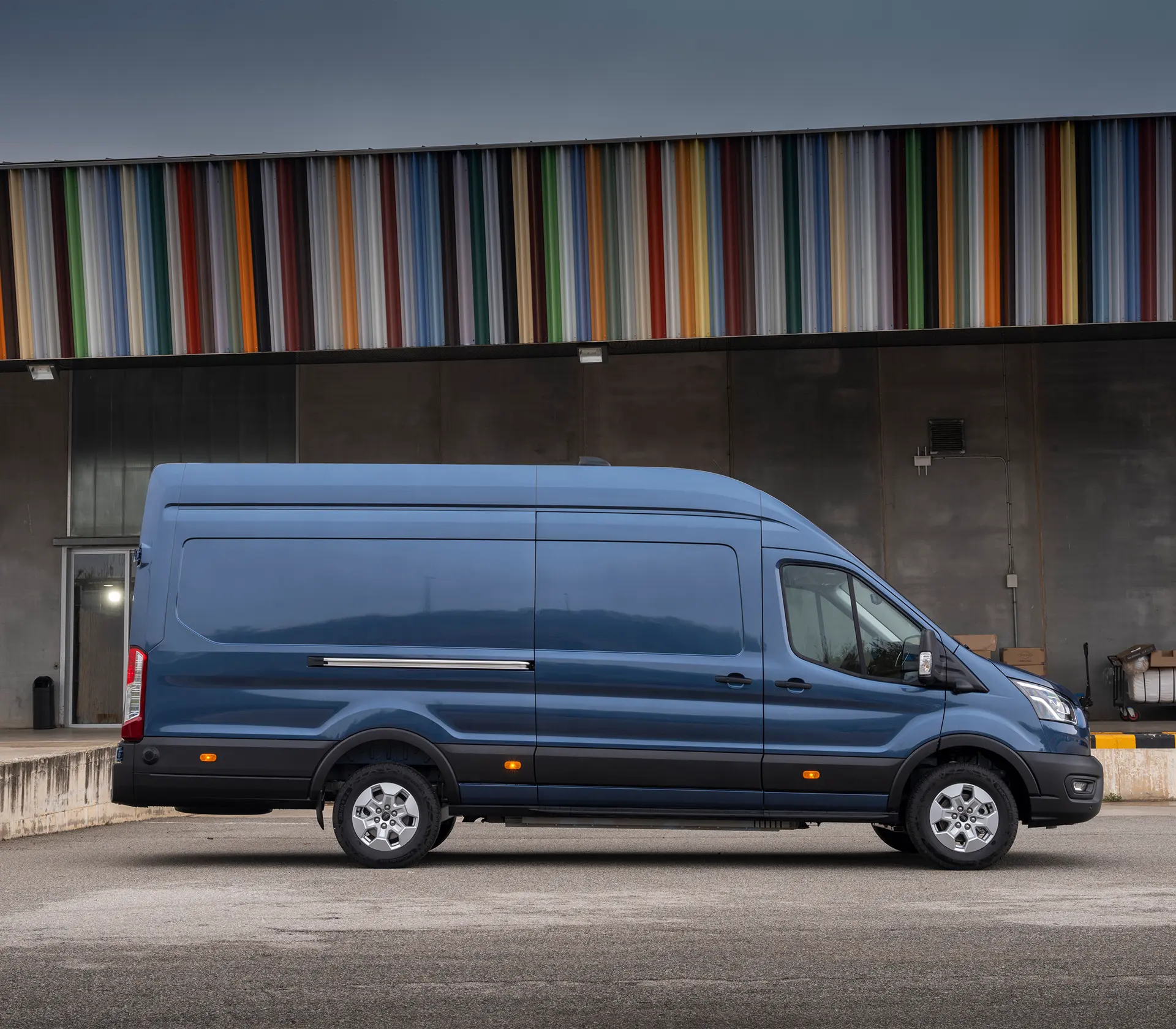 blauer E-Transit steht seitlich mit Bunten Dach im Hintergrund