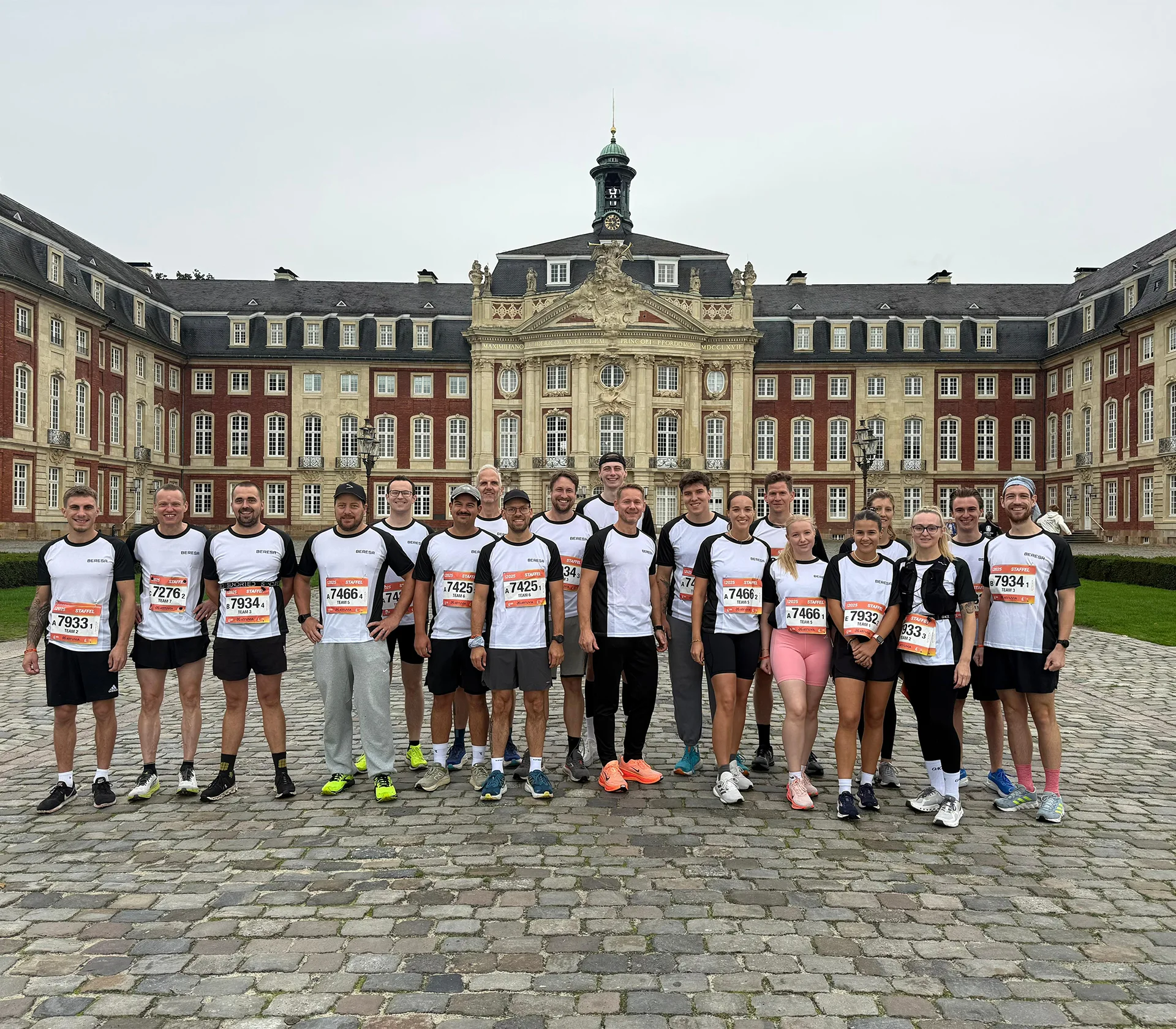 Gruppenbild vor dem Schloss in Münster vor dem Staffellauf von BERESA Mitarbeitern. Alle tragen das selbe weiß/schwarze T-Shirt mit der jeweiligen Startnummer.