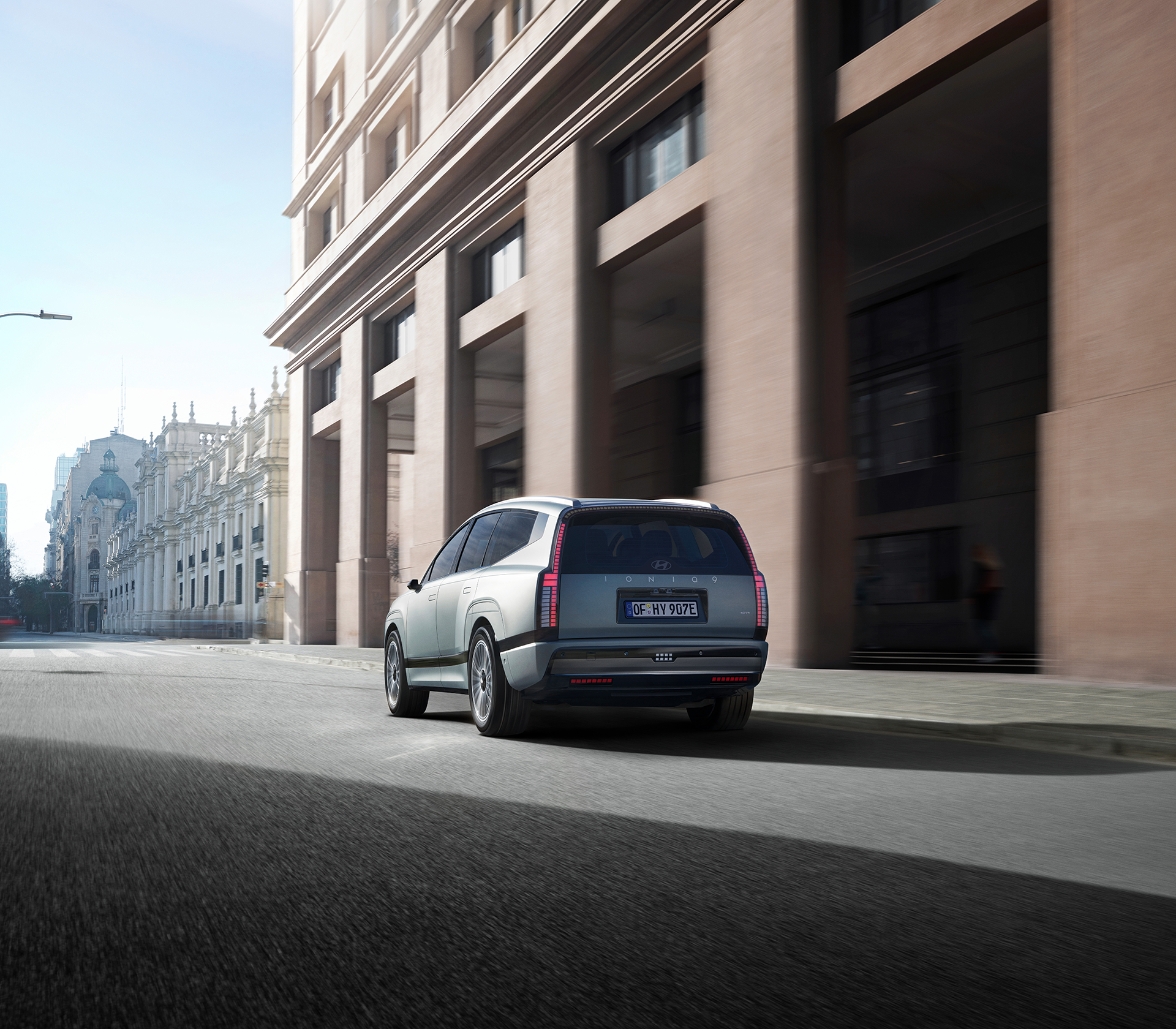 Hyundai IONIQ 9 Heckansicht, fährt durch eine Straße mit einem Gebäude im Hintergrund