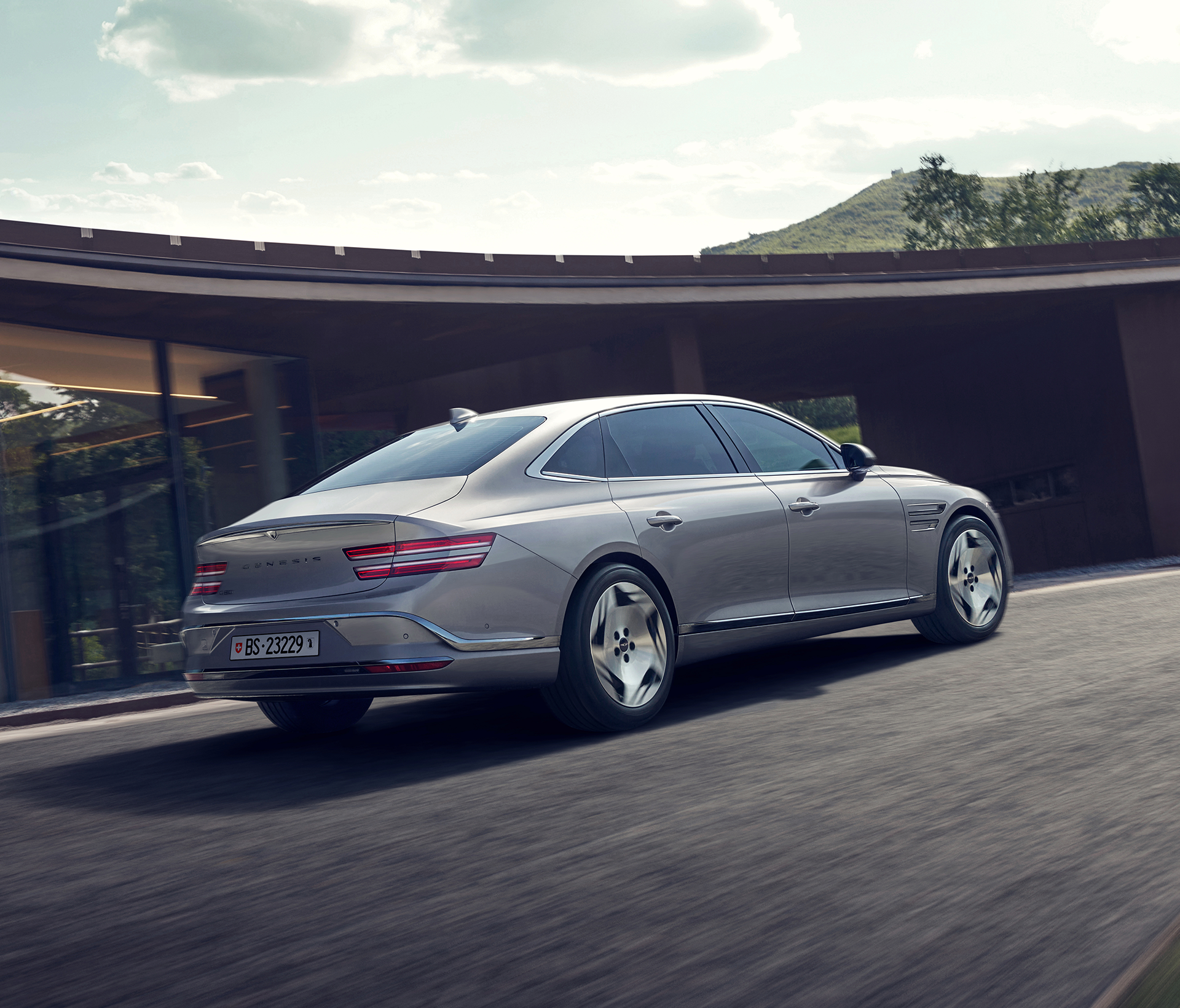 Genesis Electrified G 80 Heck und Seitenansciht während das Auto vor einer Gebäudewand fährt.