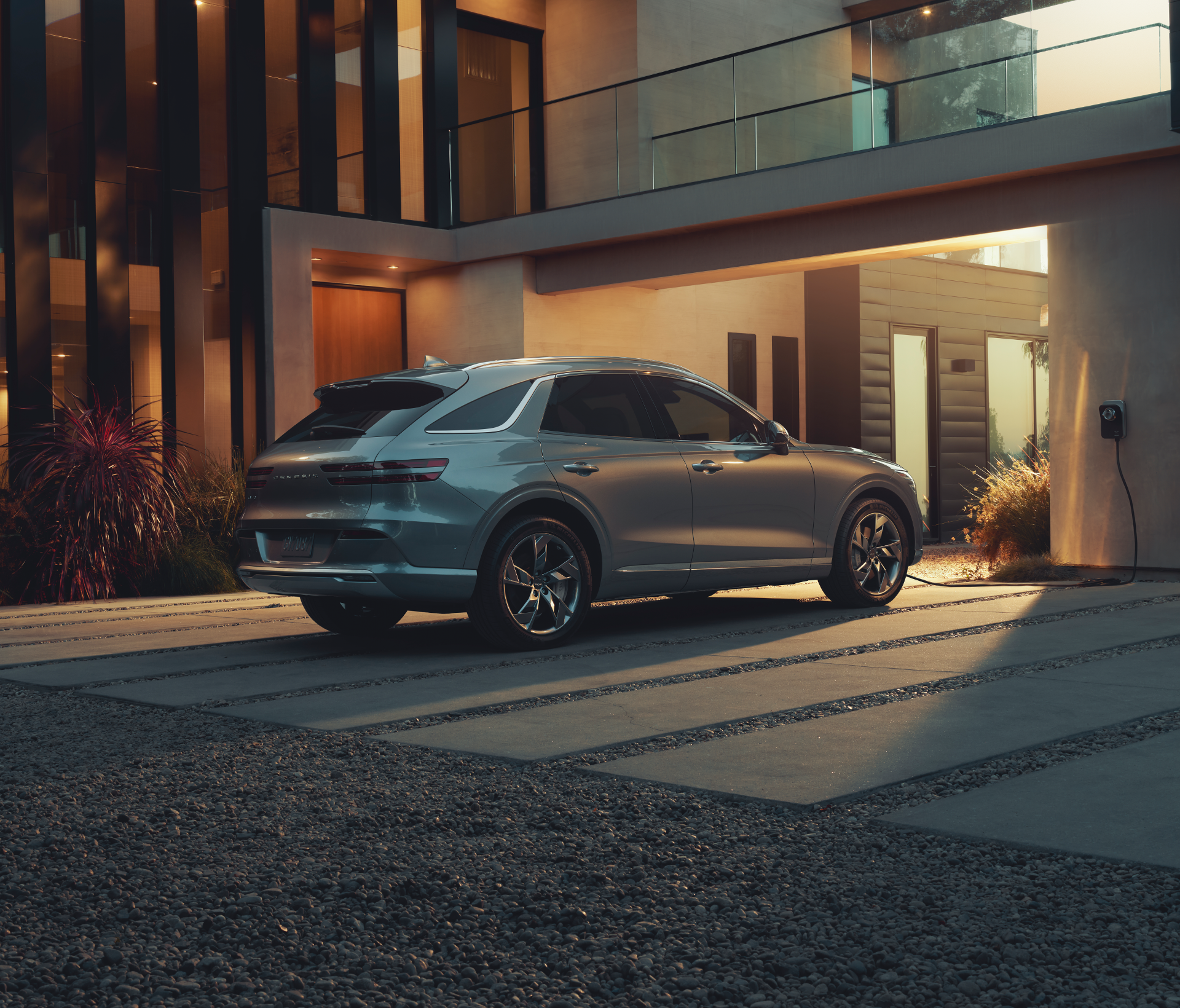 Genesis Electrified GV 70 in grau steht vor der Einfahrt eines modernen Wohnhauses.