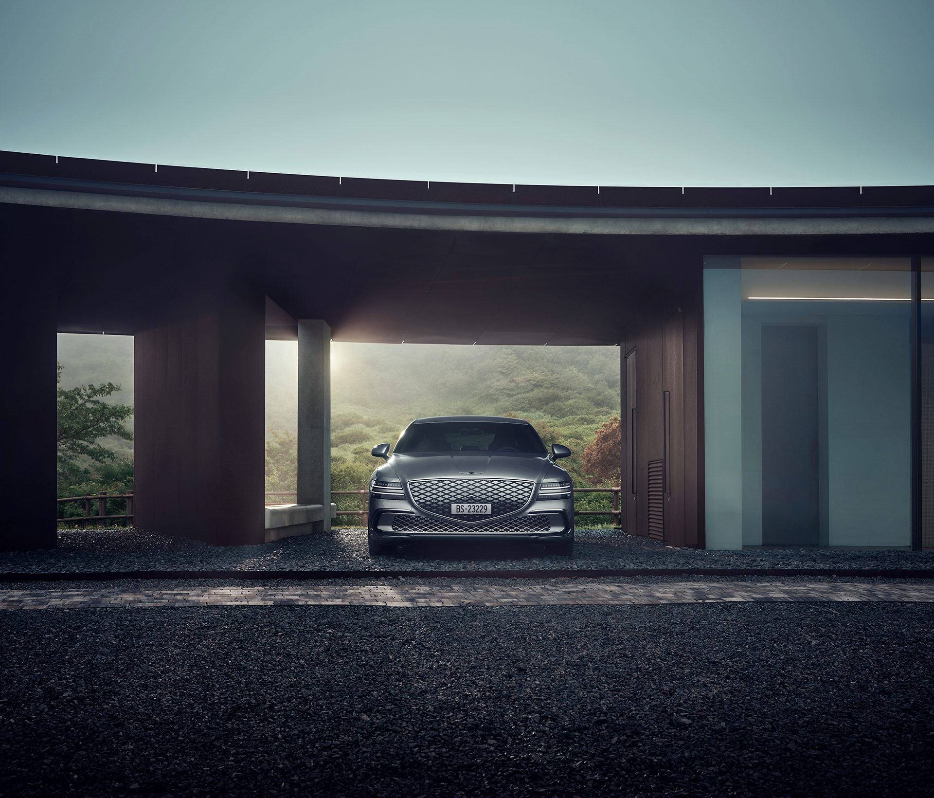 Genesis Electrified G 80 steht unterdacht bei einem modernen Haus mit dem Sonnenuntergang im Hintergrund.